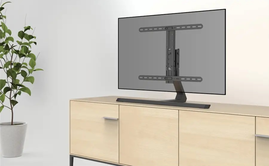 Telewizor na drewnianej szafce. Roślina w doniczce po lewej. Telewizor jest szary, a szafka jasnobrązowa.