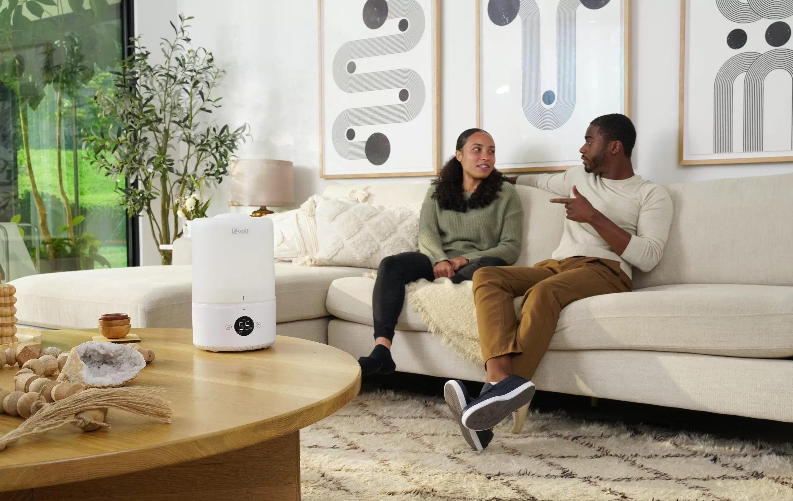 Para siedzi na kanapie. Nawilżacz powietrza stoi na stole przed nimi. Mężczyzna wskazuje.