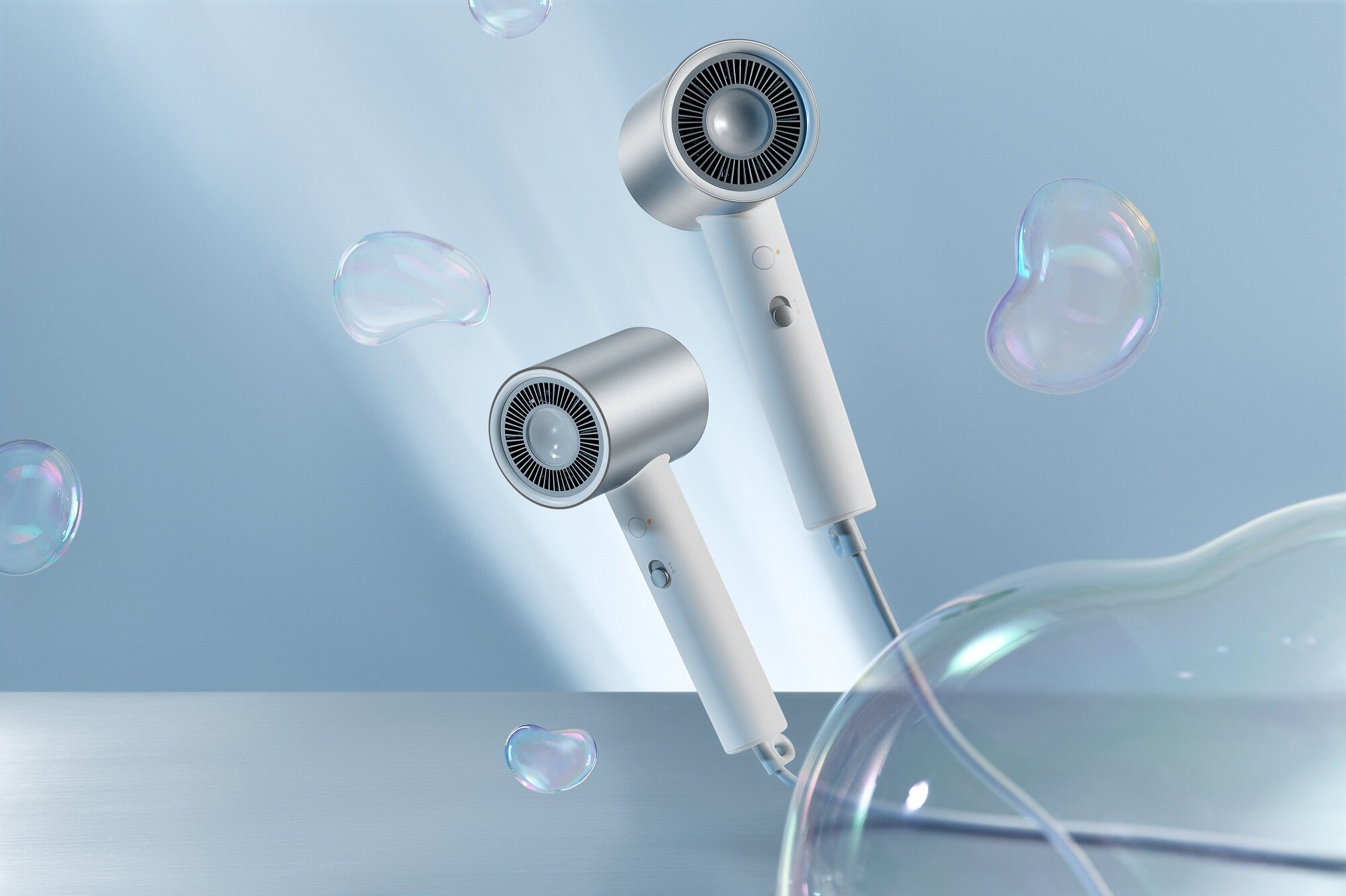 Dwie nowoczesne srebrno-białe suszarki do włosów z bąbelkami unoszącymi się na niebieskim tle.