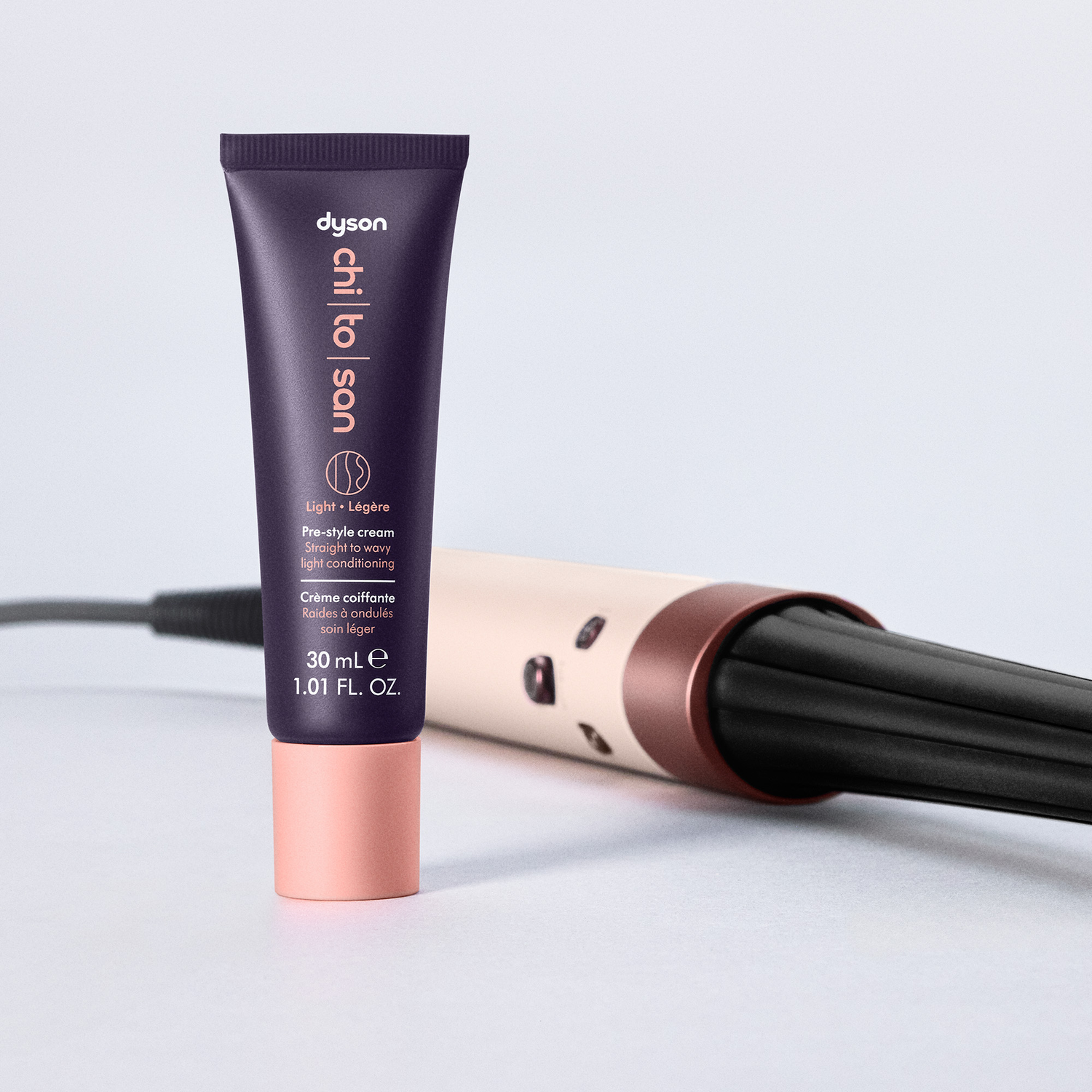 A purple Dyson Chi to Son pre-style cream tube and a curling iron are on a white background. The tube has pink accents.