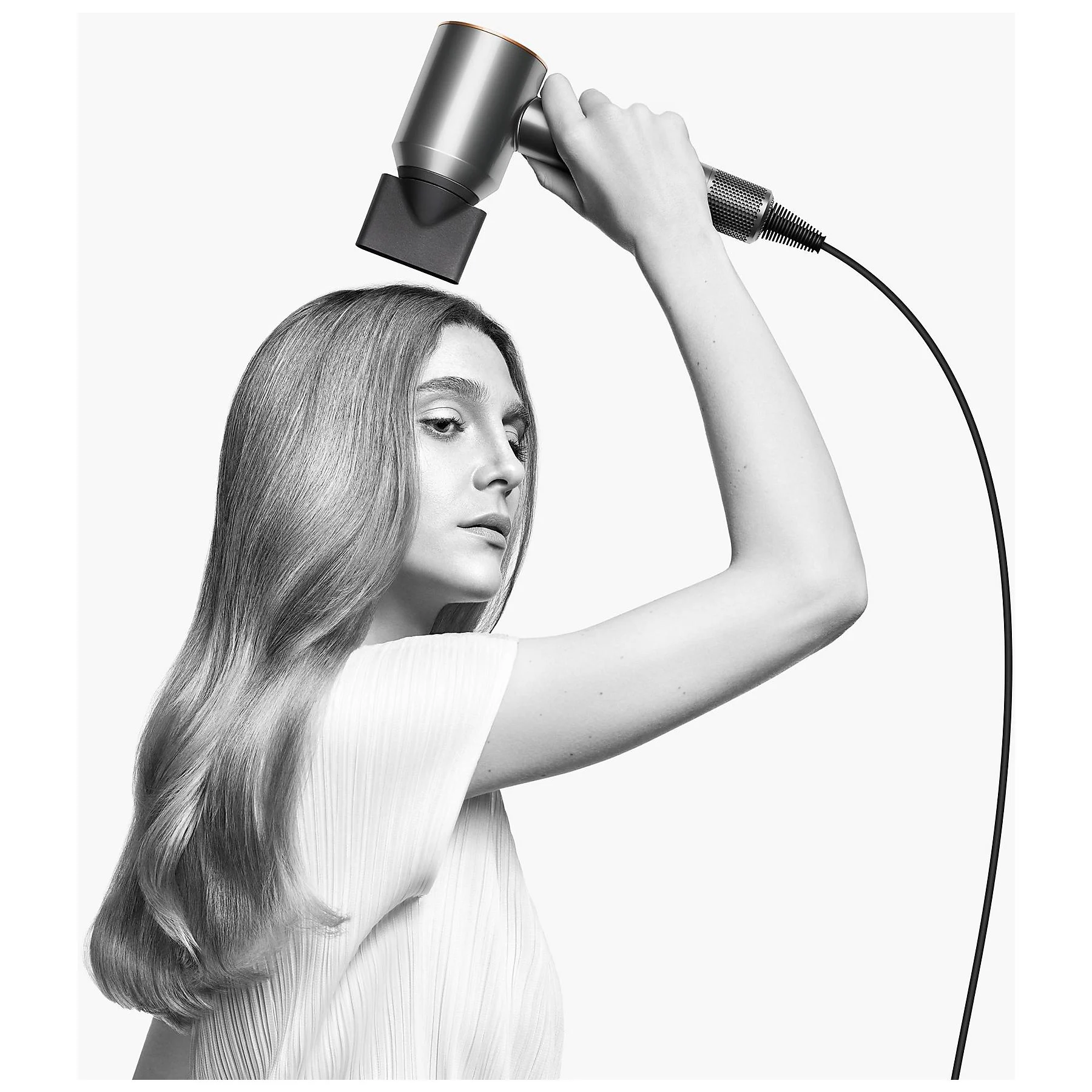 Kobieta trzyma suszarkę do włosów blisko swoich włosów. Obraz jest czarno-biały.