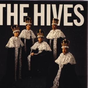 Die Bandmitglieder von The Hives in weißen Umhängen, Kronen und schwarzen Outfits. Der Bandname steht darüber.