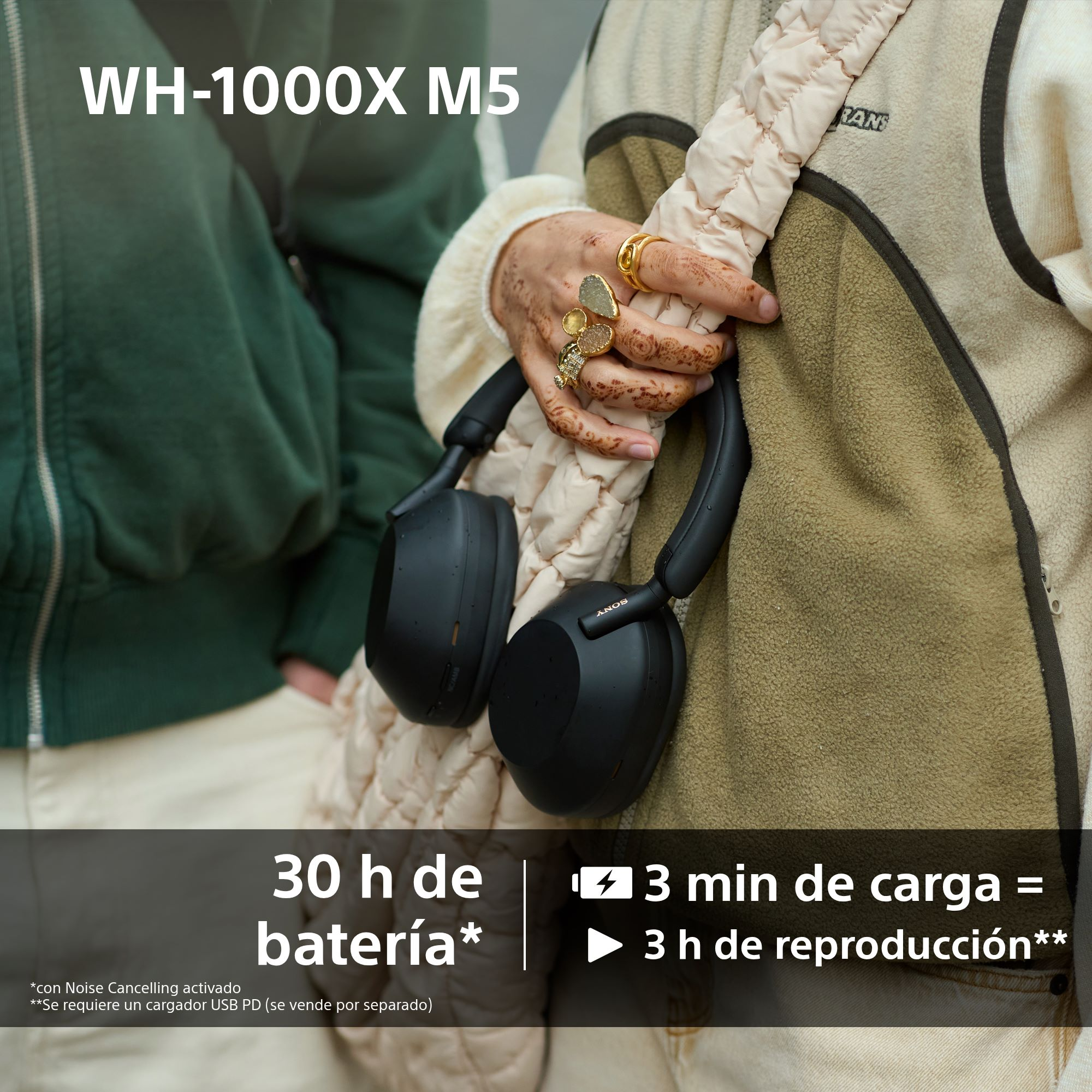 Persona sosteniendo auriculares Sony negros. El fondo tiene una chaqueta verde y una chaqueta beige. Texto sobre la duración de la batería.