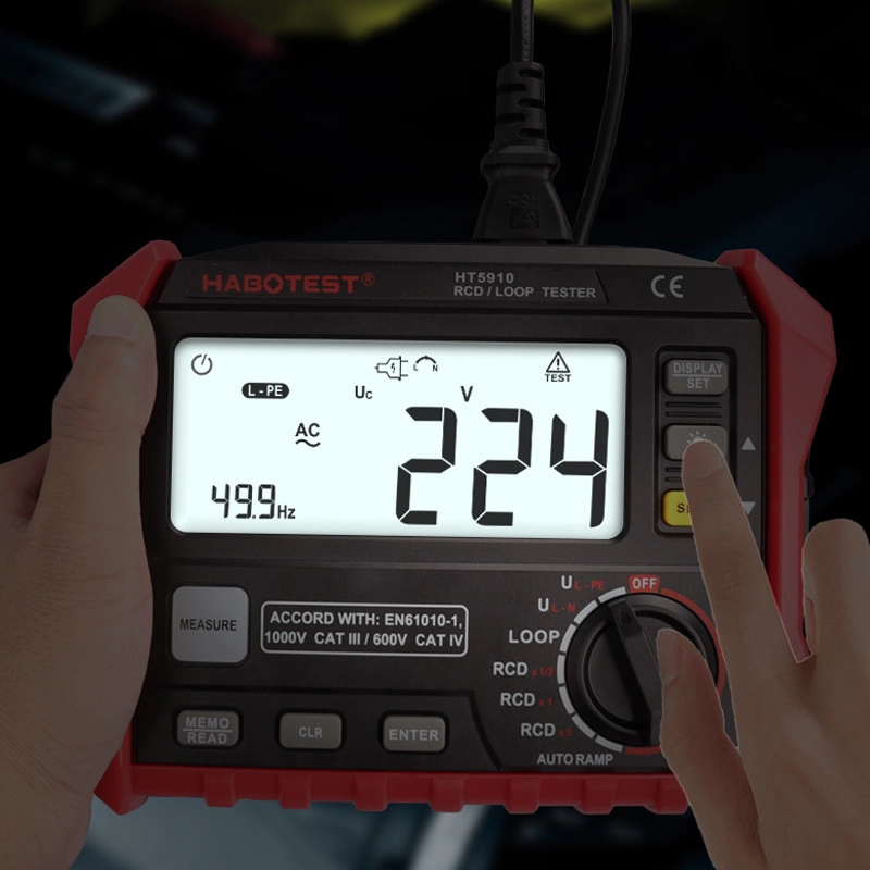 Egy kéz egy piros-fekete elektromos tesztert tart, ami 224 V-ot és 49,9 Hz-et mutat. Egy másik kéz nyomja a gombokat az eszközön.