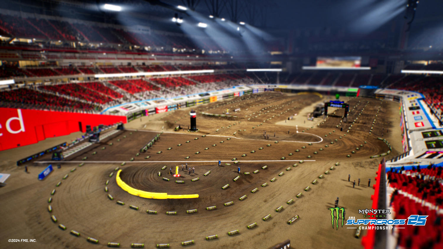 Eine Indoor-Motocross-Strecke mit Sprüngen und Kurven. Rote Sitzplätze umgeben die Strecke. Logos und Branding sind sichtbar.