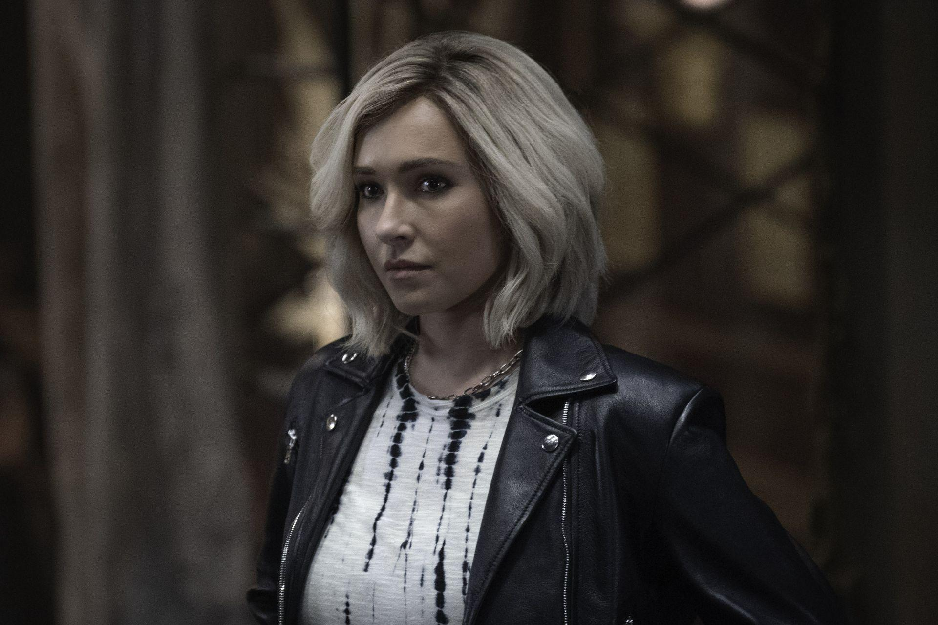 Frau mit blonden Haaren, trägt eine schwarze Lederjacke und ein Batik-Shirt. Sie schaut leicht nach links, drinnen.
