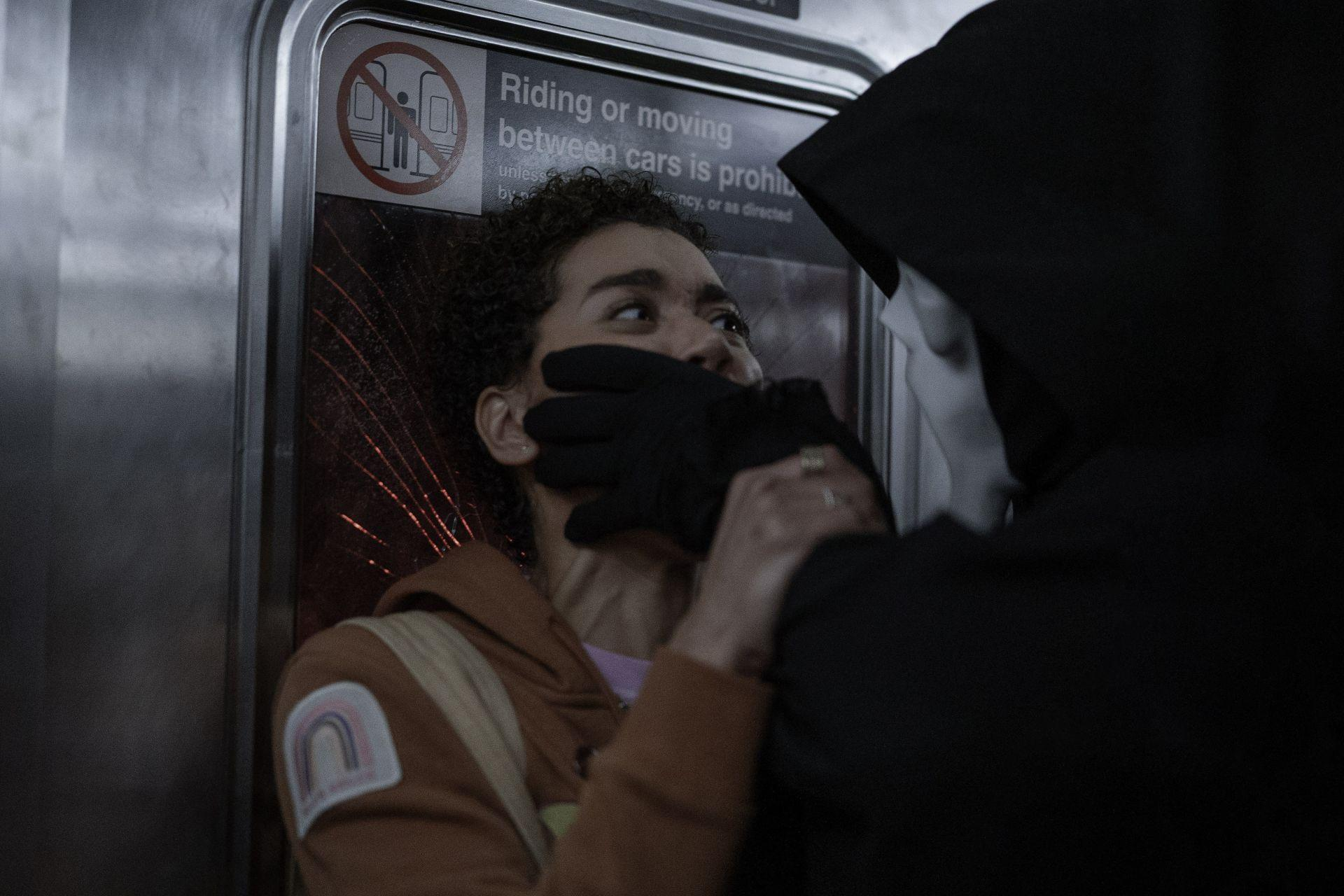Eine Person wird in einer U-Bahn angegriffen. Eine maskierte Gestalt mit einem schwarzen Handschuh bedeckt den Mund des Opfers.
