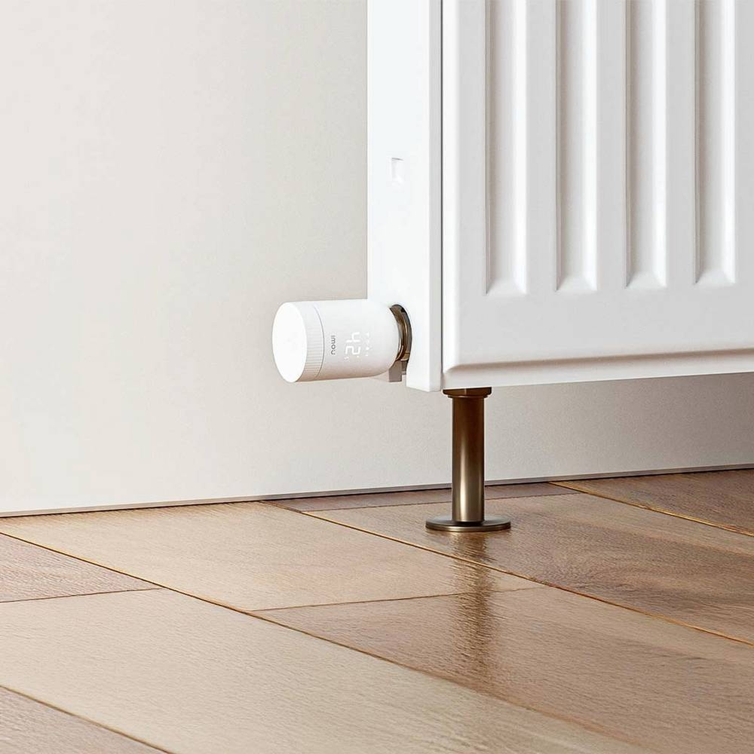 A white radiator with a smart thermostat attached. The thermostat displays 42. The radiator is on wooden flooring.