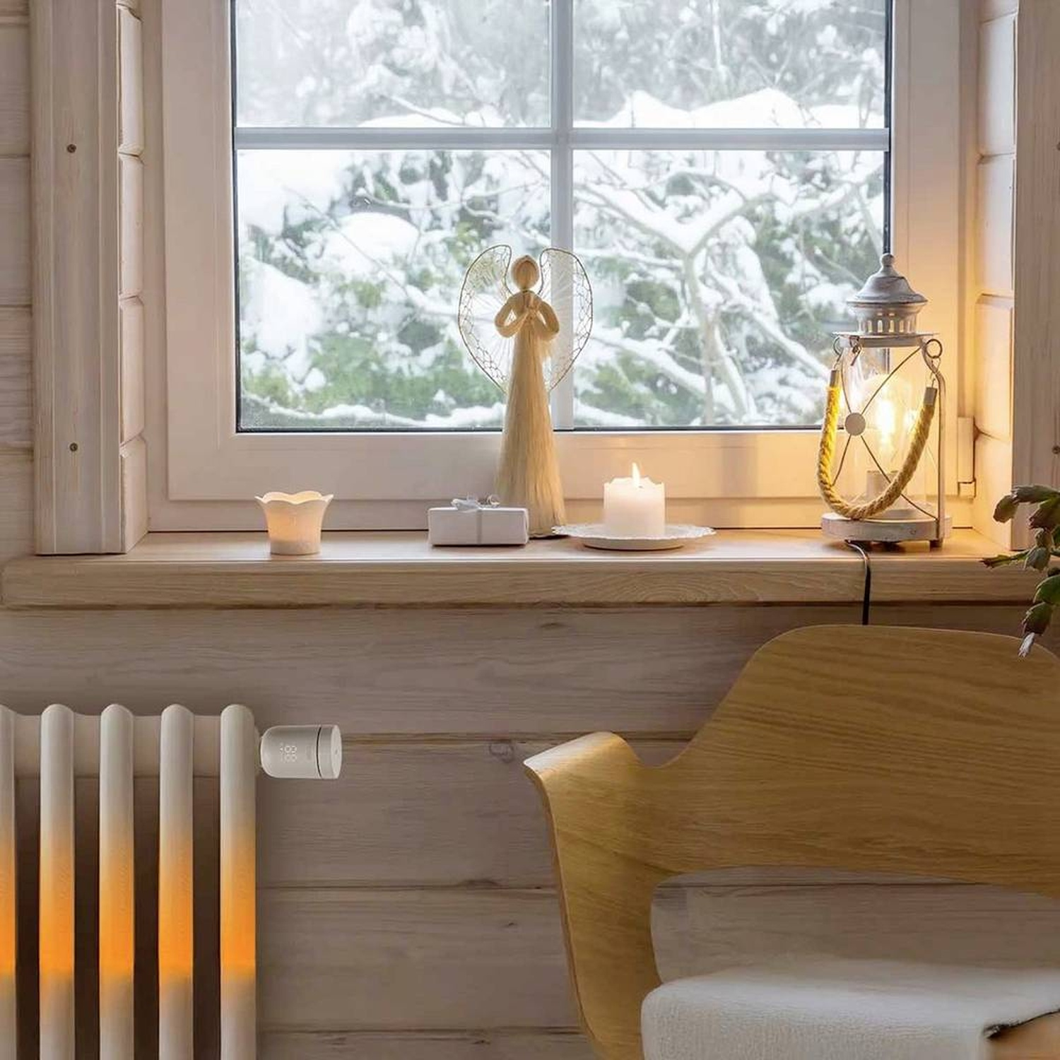Cozy interior scene: window with snowy view, angel, candle, lantern, radiator, wooden chair. Warm light and winter atmosphere.