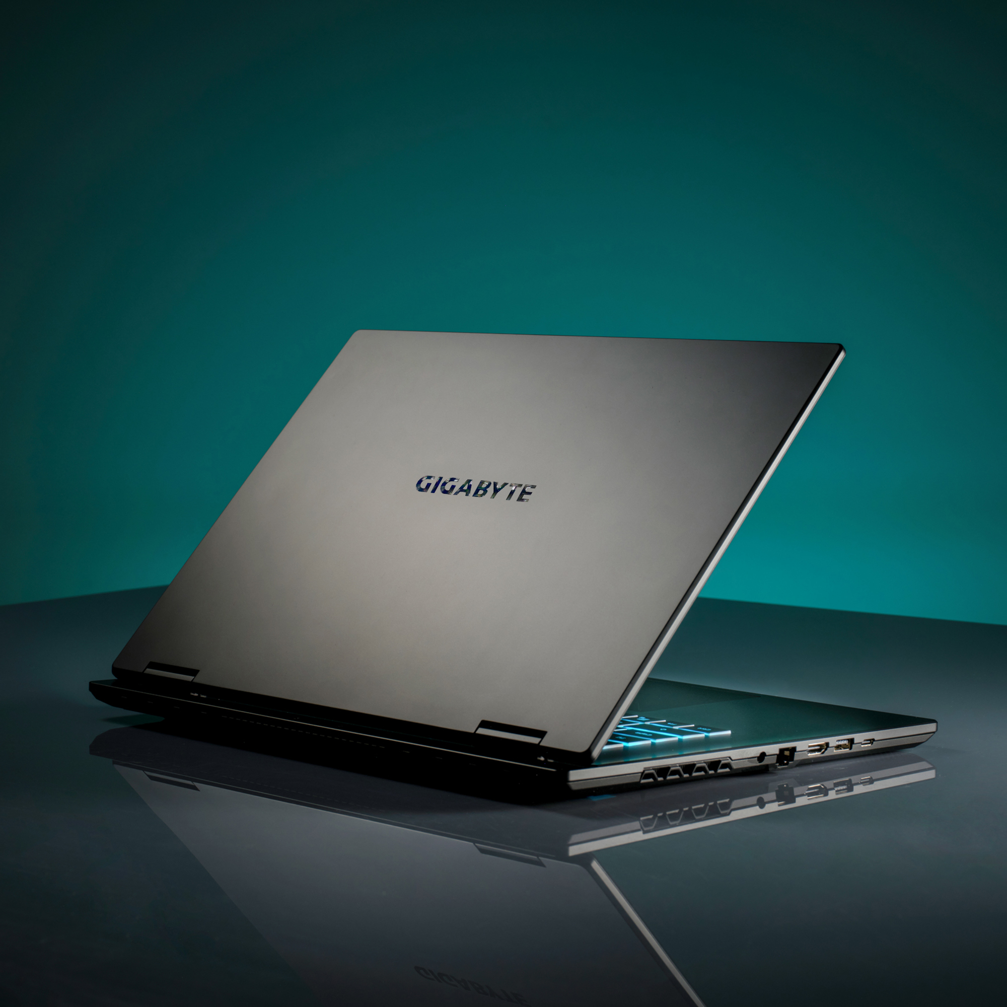 Ein schwarzer Laptop steht auf einer reflektierenden Oberfläche. Der Bildschirm ist geöffnet und zeigt beleuchtete Tasten. Der Hintergrund ist türkis.