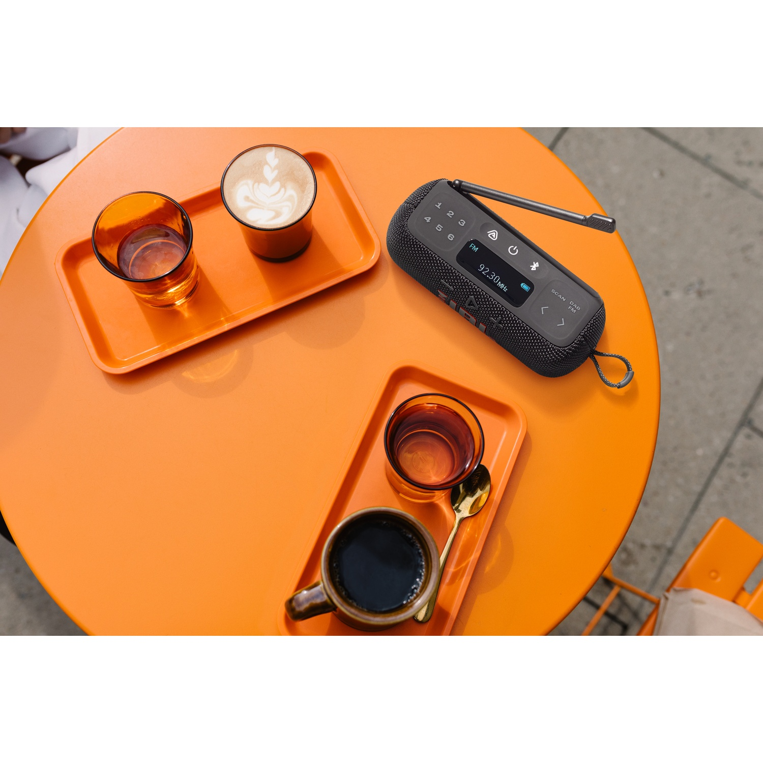 Een oranje tafel met koffie, een luidspreker en drankjes. Twee trays bevatten koffie en drankjes. Een luidspreker staat op de tafel.