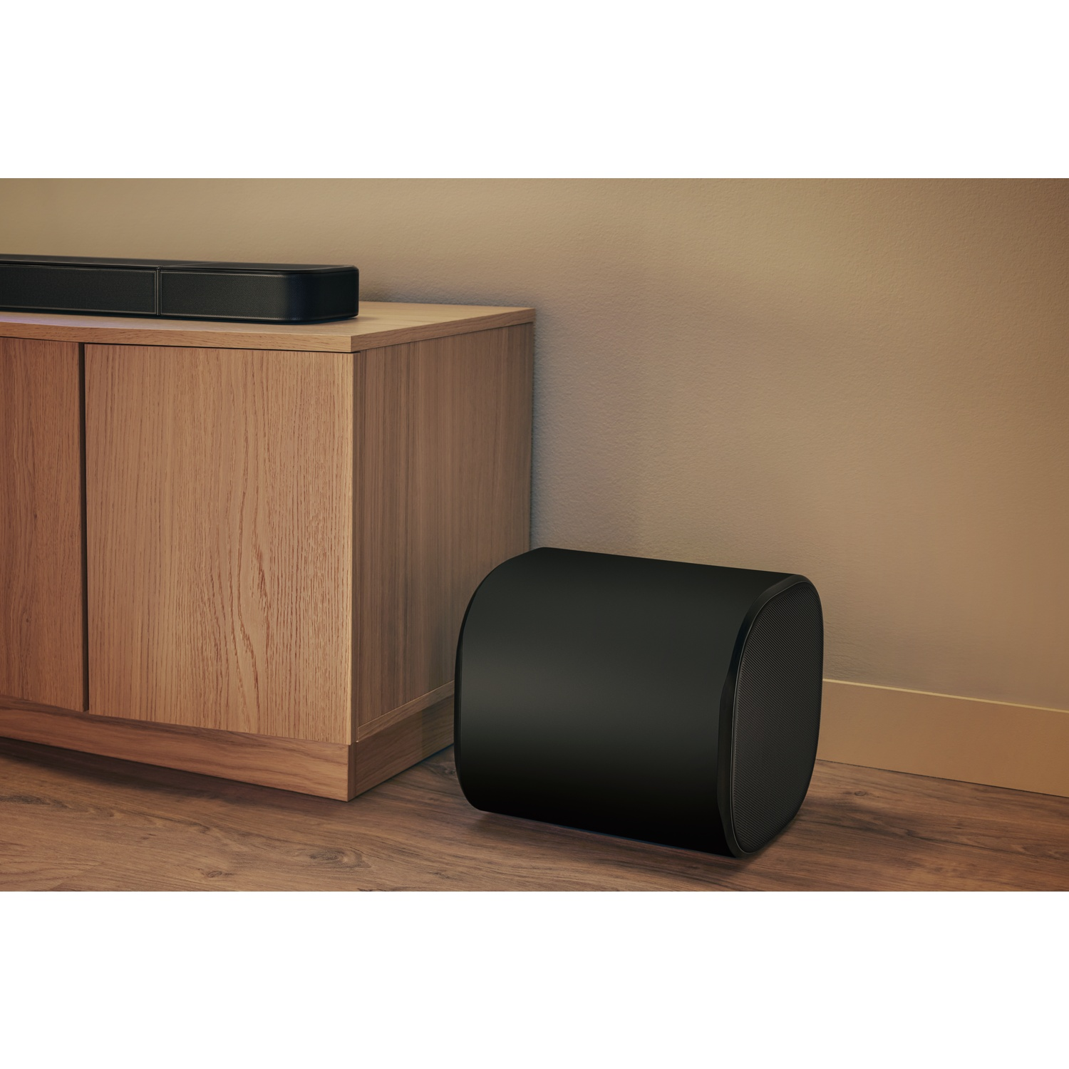 Un haut-parleur noir est posé sur un plancher en bois. Une armoire en bois avec une barre de son est contre un mur beige.