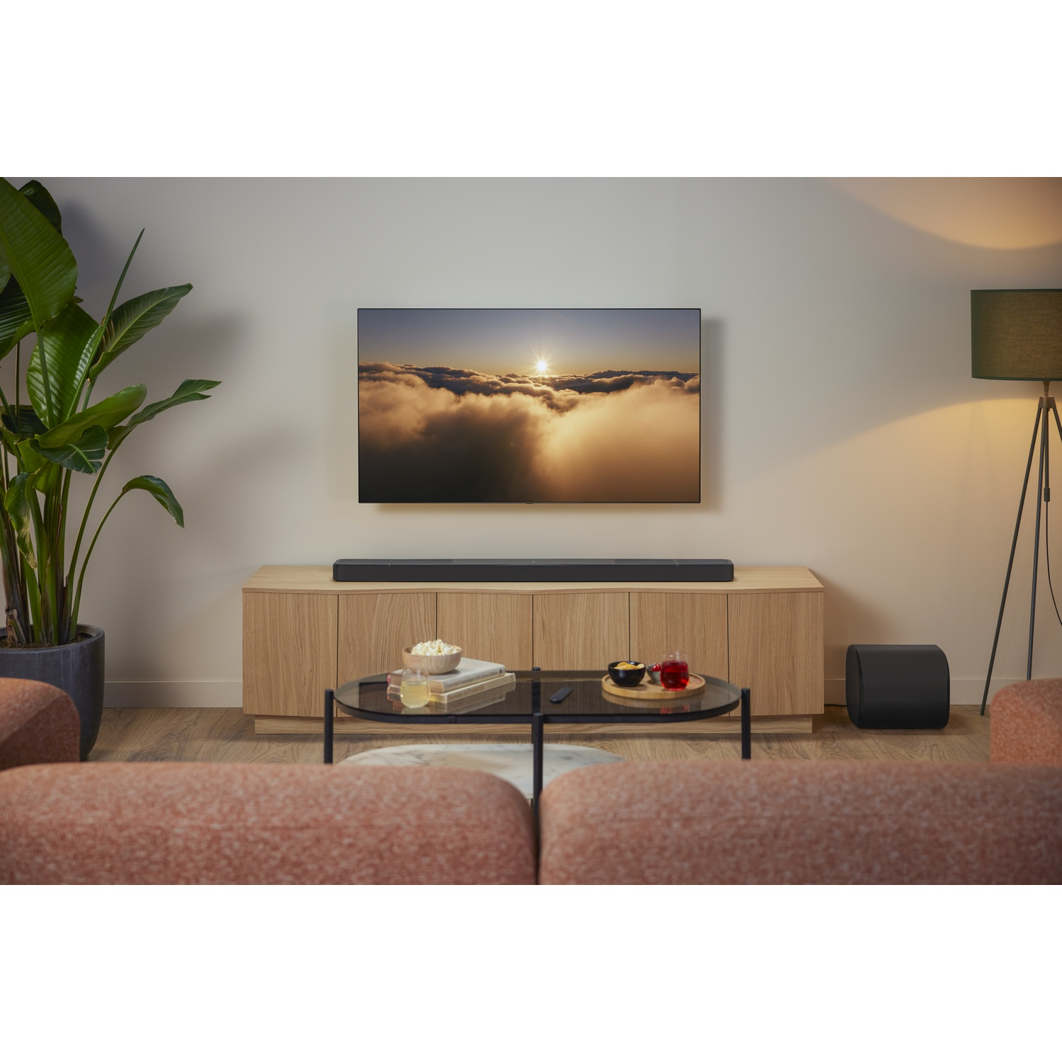 Salon avec TV montrant des nuages, barre de son, meuble en bois, table basse avec collations et canapé.