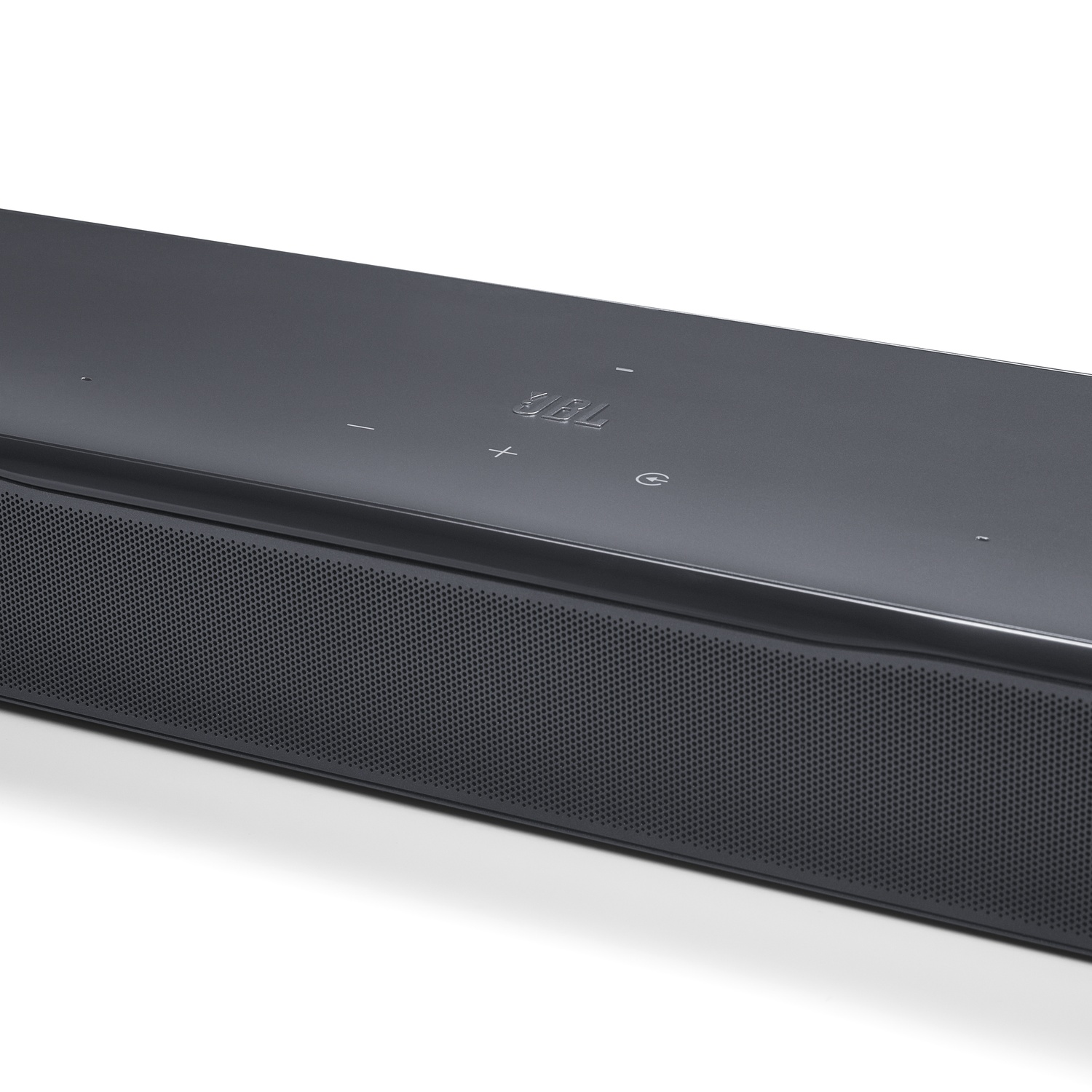 Une barre de son JBL gris foncé sur fond blanc. Elle a une façade en mesh et des boutons de commande sur le dessus.