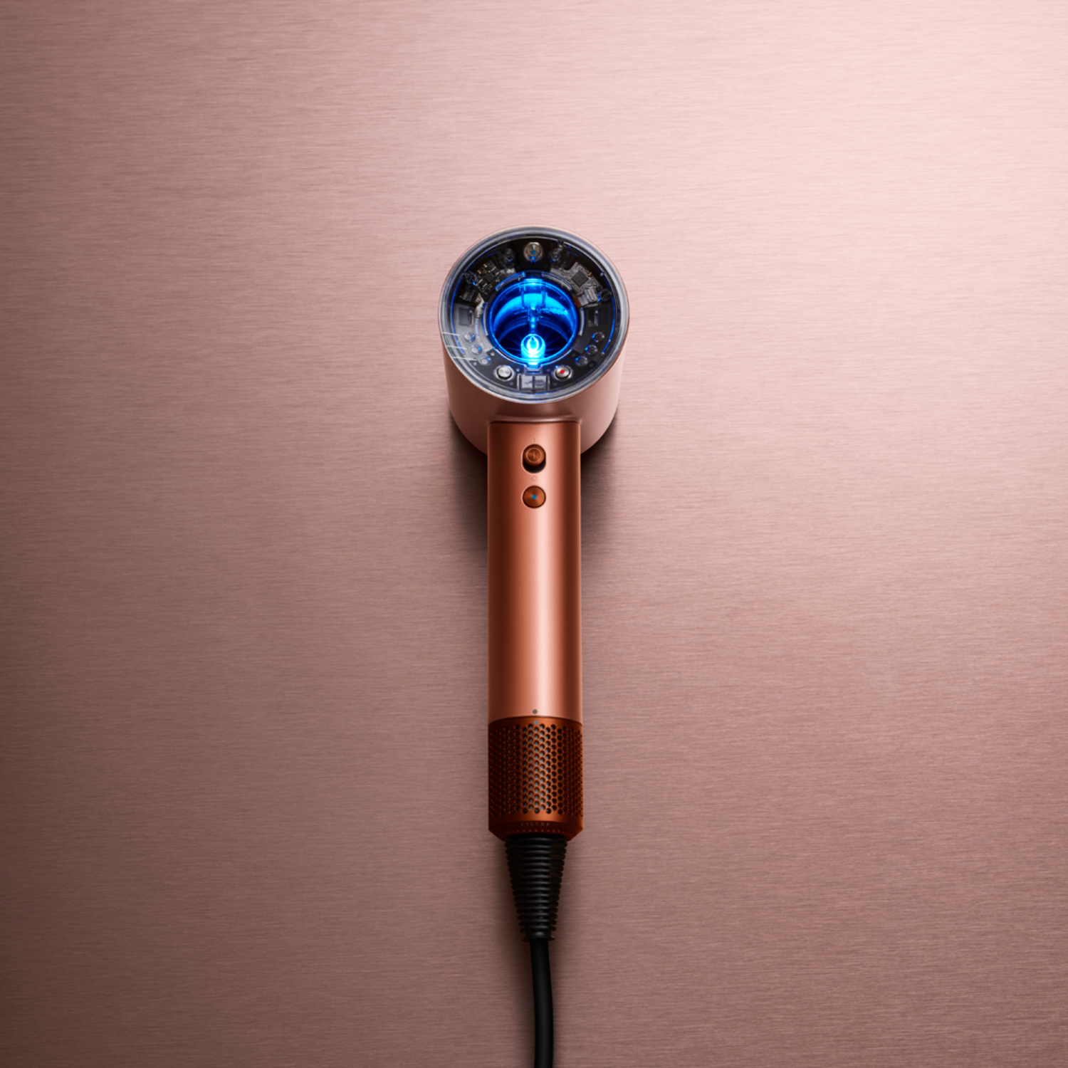 Copper-colored Dyson hair dryer on a copper background. The dryer has a blue light in the head and a black power cord.