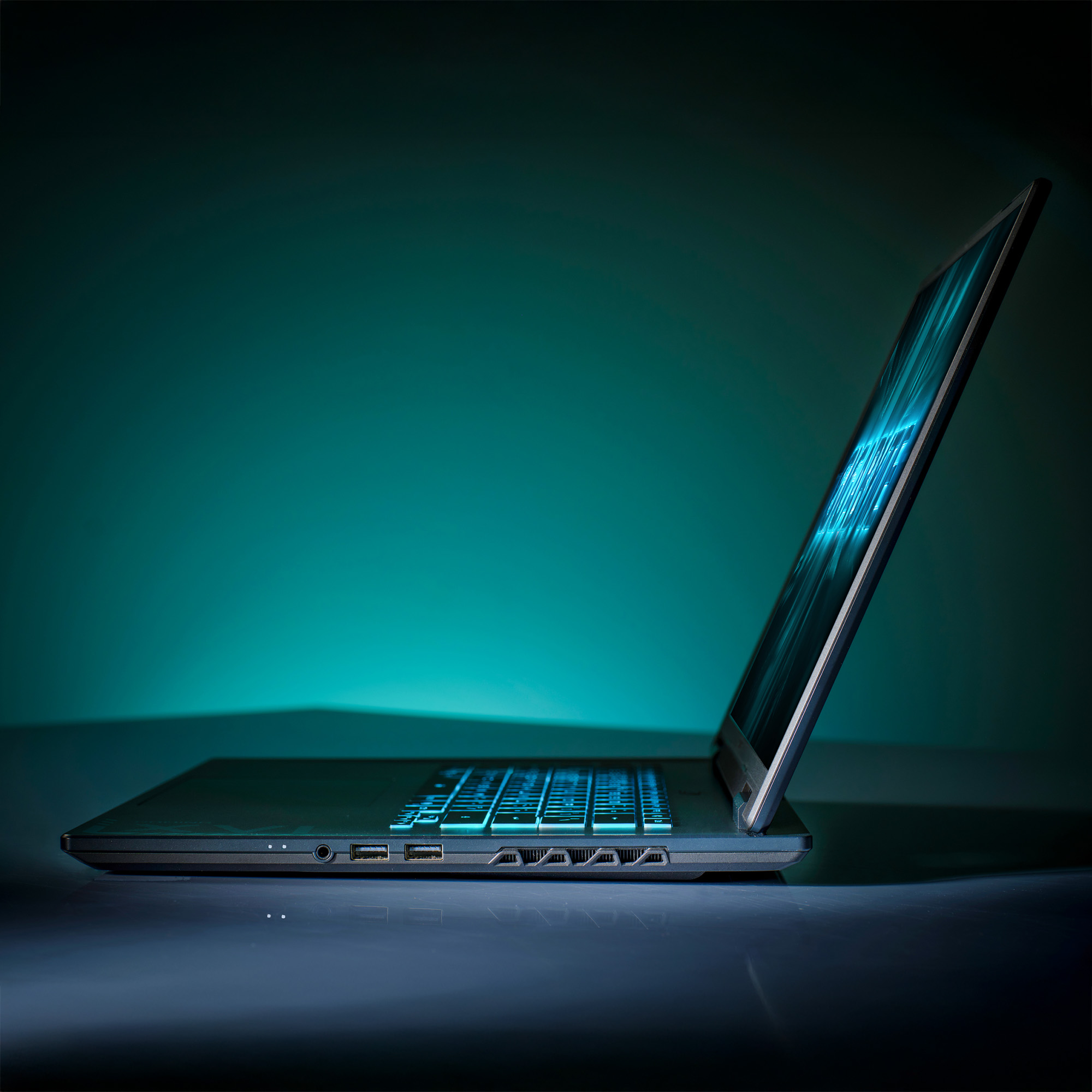 Laptop, leicht geöffnet, auf einer reflektierenden Oberfläche. Tastatur leuchtet blau. Der Bildschirm zeigt blauen Text.