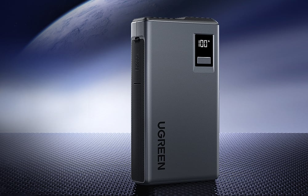 Sötétszürke UGREEN power bank, 100%-ot mutató digitális kijelzővel. A háttérben űrszerű jelenet és texturált felület látható.