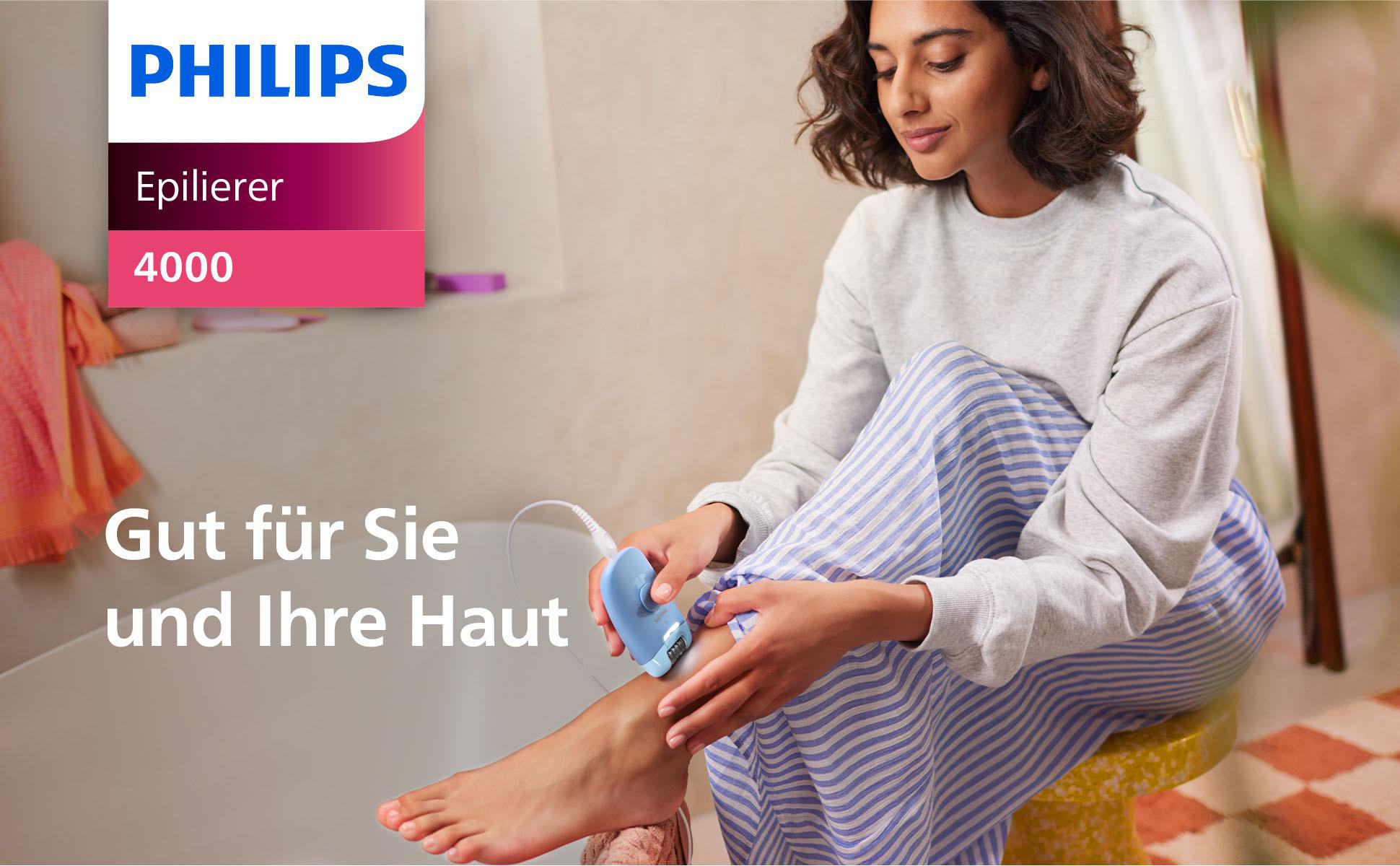 Frau epiliert Bein. Sie trägt graues Oberteil und blau gestreifte Hose, sitzt auf gelbem Hocker. Philips Logo sichtbar.