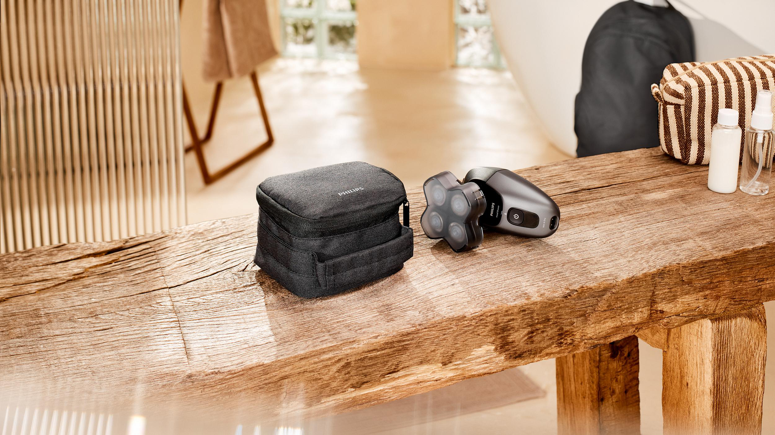 Auf einer Holzbank liegen ein Philips-Rasierer, eine Reisetasche und Toilettenartikel. Im Hintergrund ist ein Badezimmer zu sehen.