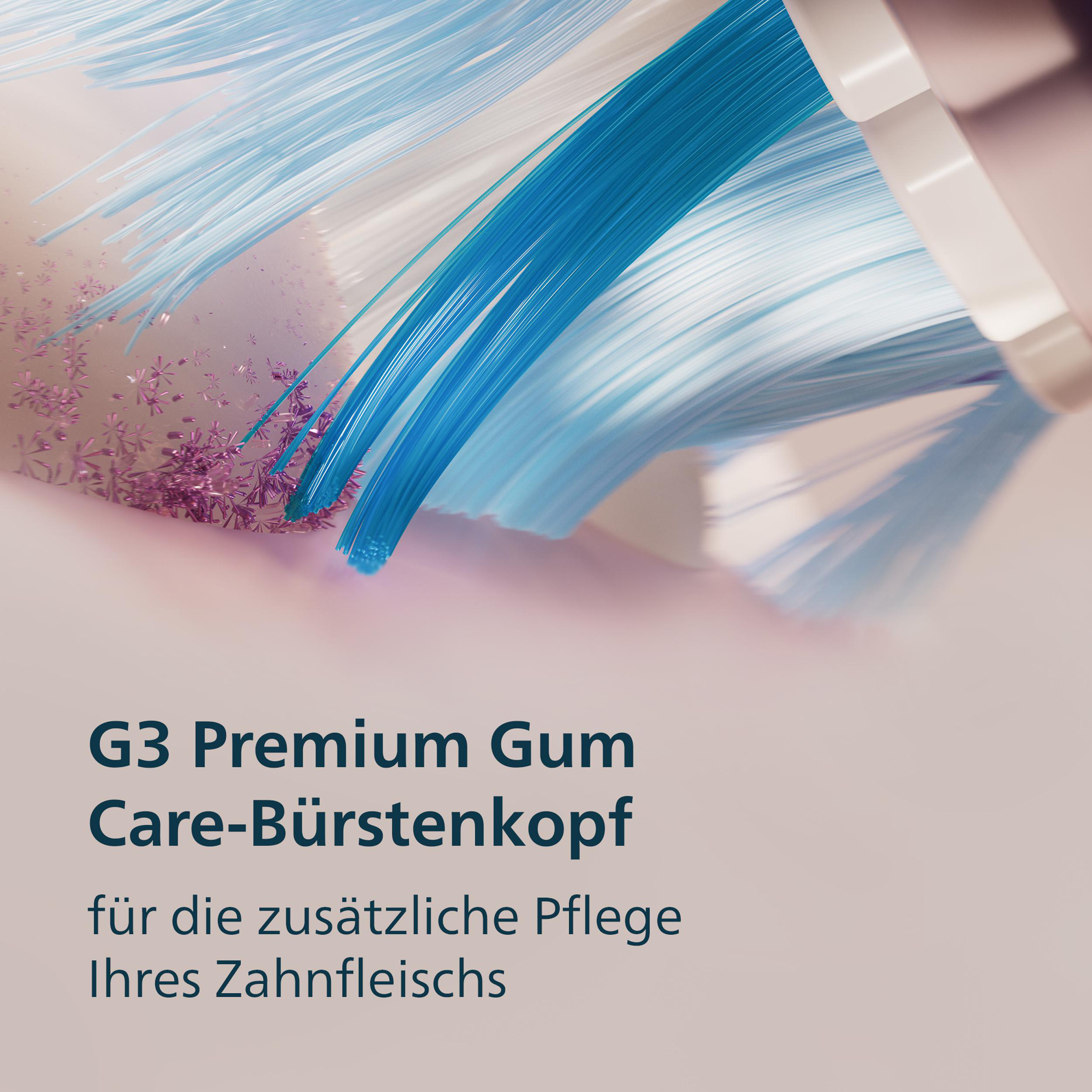 Nahaufnahme eines Zahnbürstenkopfes mit blauen und weißen Borsten. Rosa Partikel auf der Oberfläche mit Text: G3 Premium Gum Care.