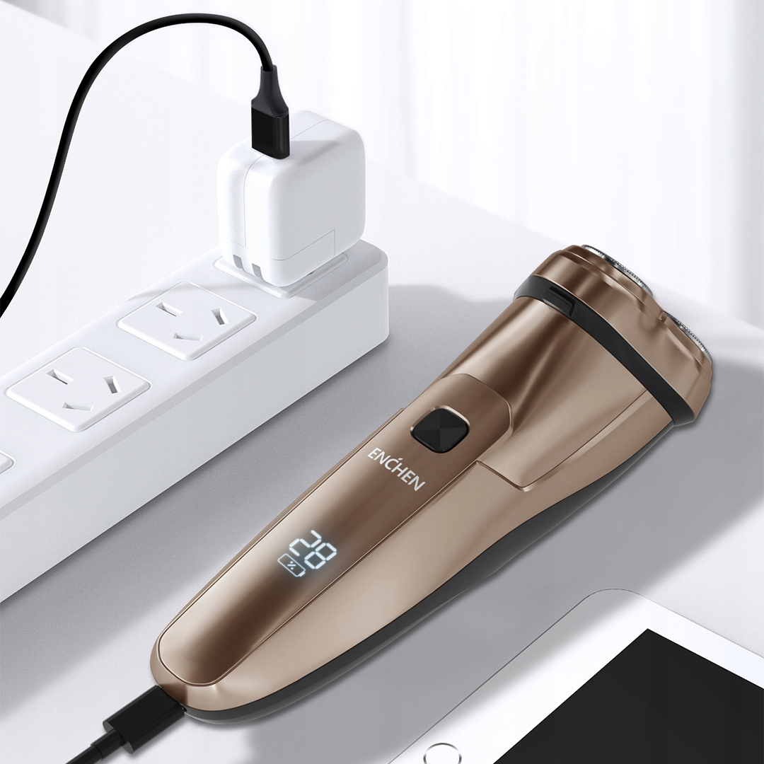 Złota golarka elektryczna ładuje się obok białej listwy zasilającej i białego zasilacza. Czarny kabel łączy golarkę z adapterem.