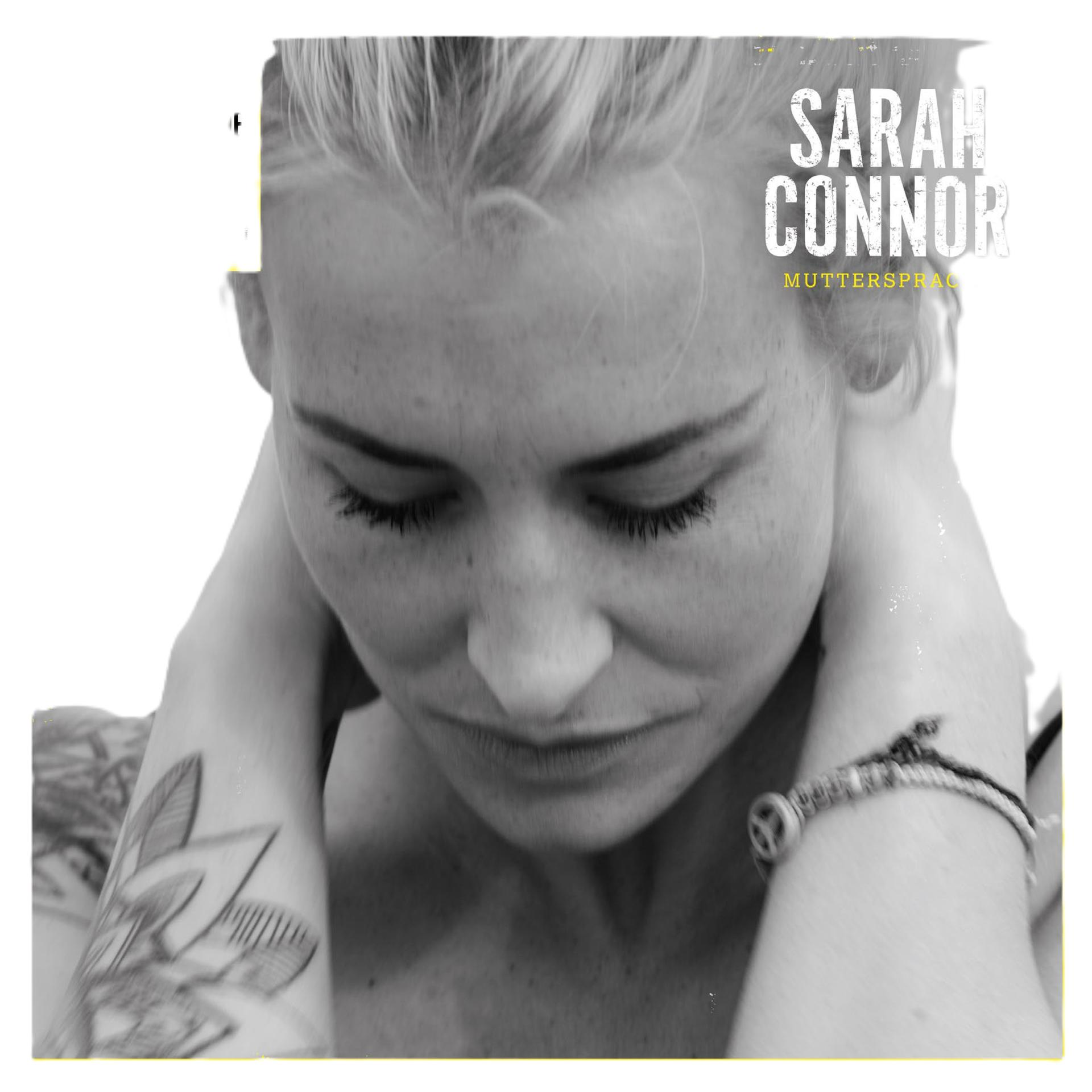 Schwarz-Weiß-Foto einer Frau mit blondem Haar, die ihre Arme um den Hals hat, ein Tattoo am Arm und ein Armband. Der Text 'SARAH CONNOR' ist sichtbar.