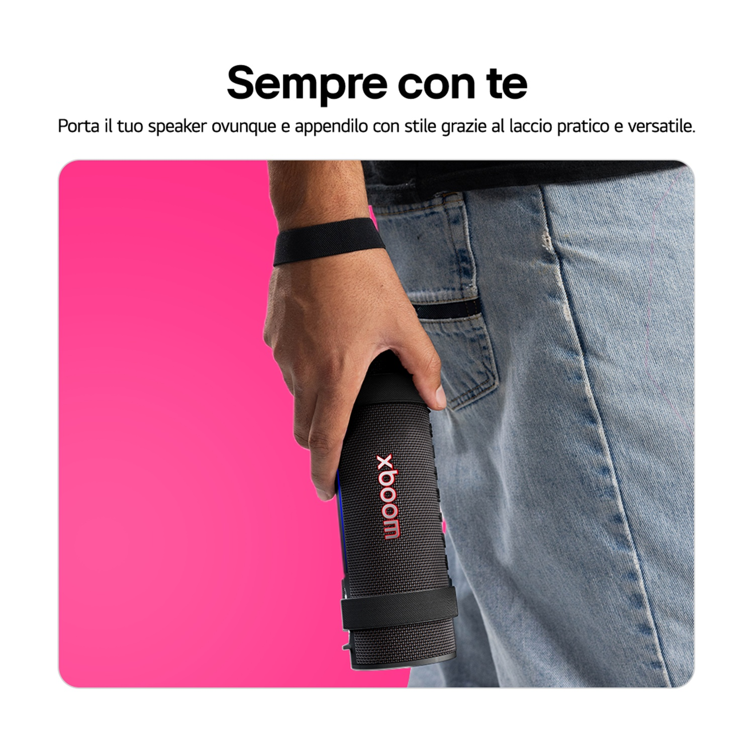 Una persona tiene in mano un altoparlante nero con il logo 'xboom'. Lo sfondo è rosa e la persona indossa jeans blu.