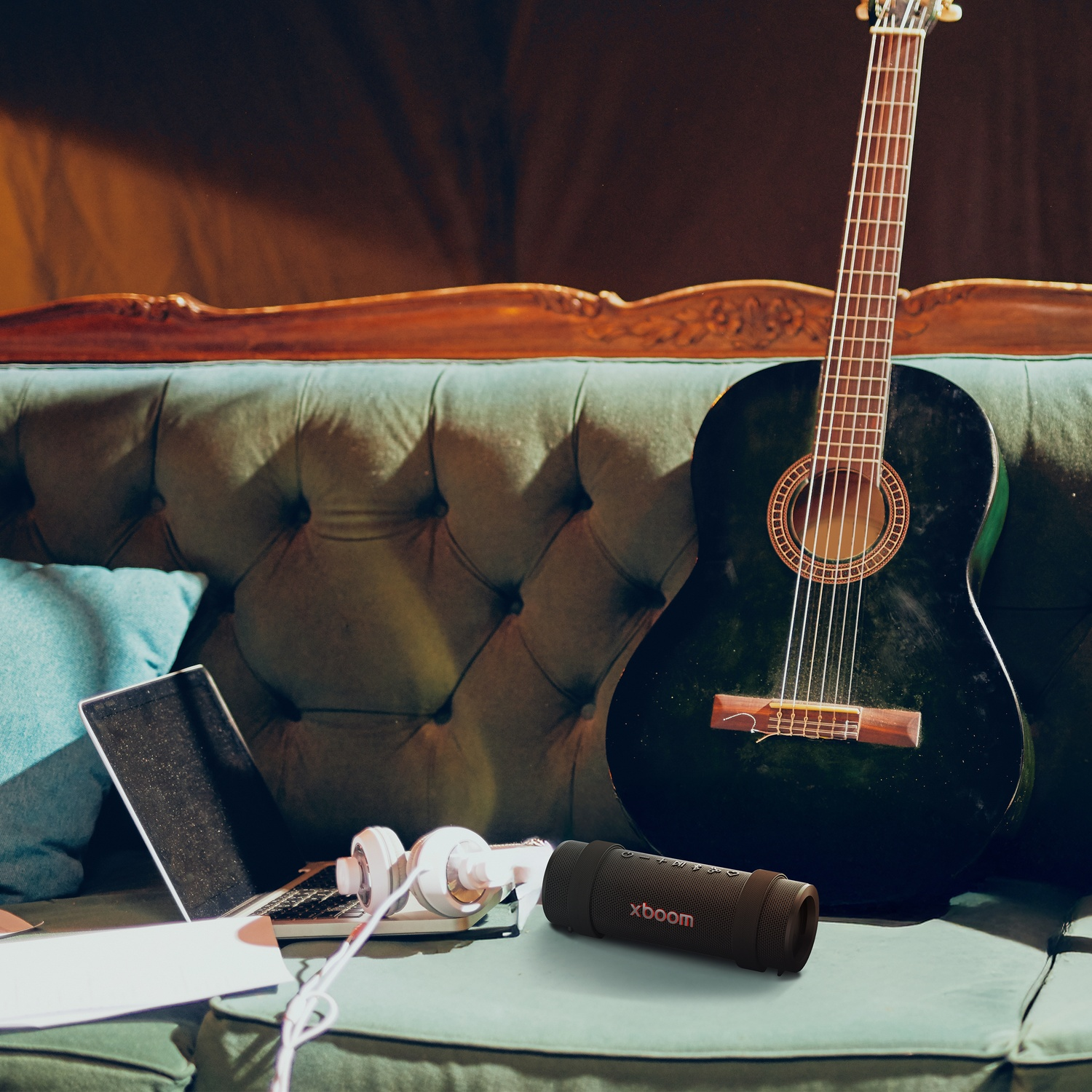La chitarra acustica è appoggiata a un divano verde. Un laptop, cuffie e un altoparlante sono sul divano.
