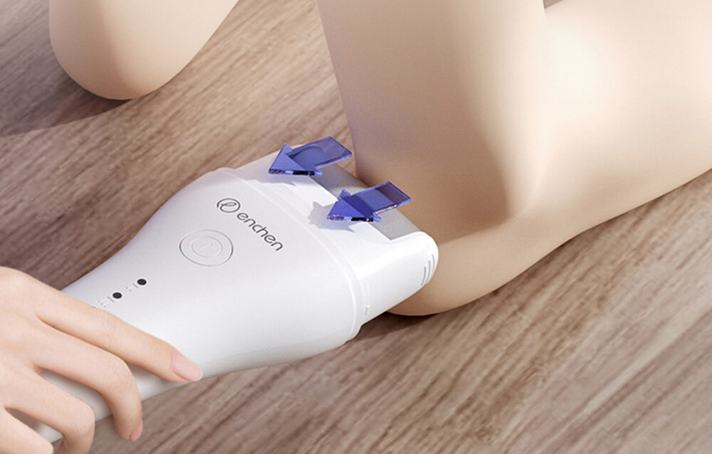 Biała golarka elektryczna jest używana na nodze. Niebieskie strzałki wskazują kierunek. Tło to drewniana podłoga.