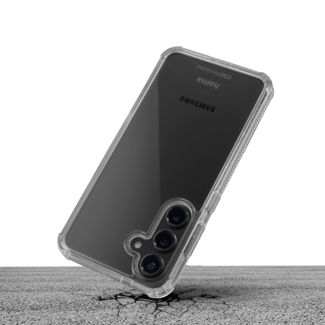Eine transparente Handyhülle schützt ein schwarzes Samsung-Handy. Das Telefon liegt auf einem rissigen Boden. Hama und D3O sind sichtbar.