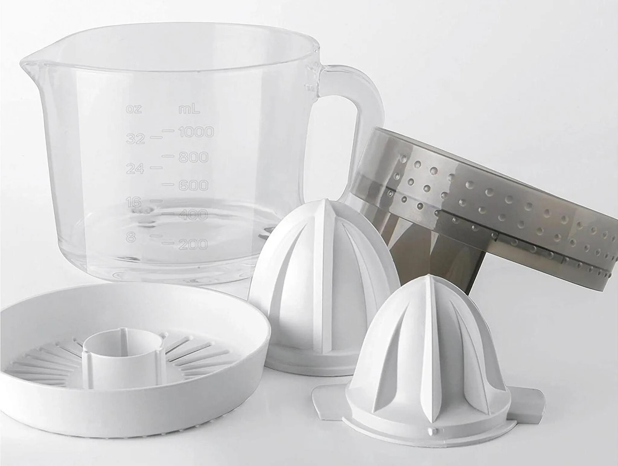 Przezroczysty kubek z miarką, białe części wyciskarki i szare sitko ułożone na białej powierzchni.