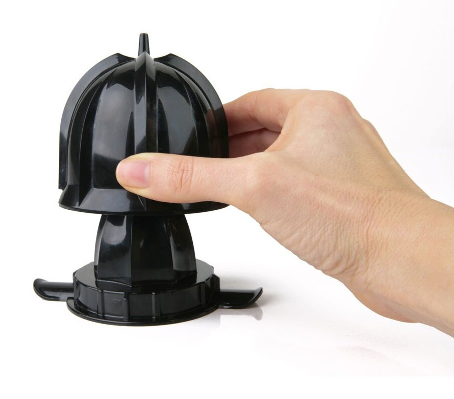 Ręka trzyma czarną wyciskarkę do cytrusów. Wyciskarka znajduje się na białym tle. Ręka jest na górnej części wyciskarki.