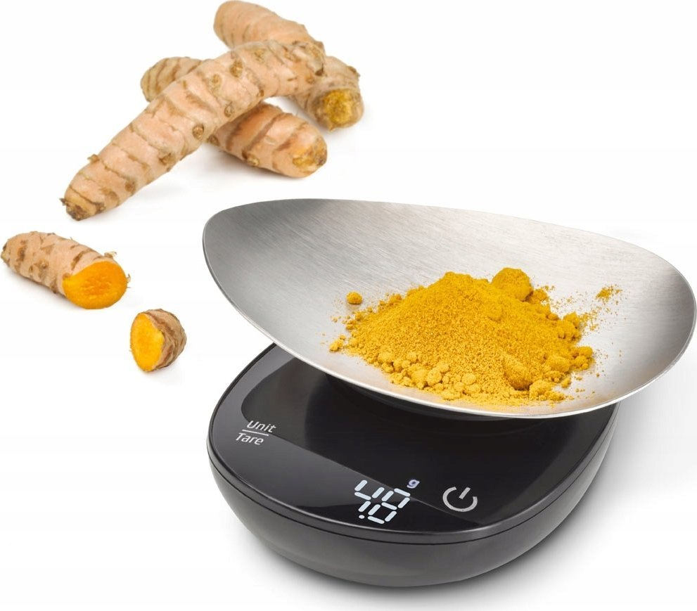 Korzenie kurkumy i proszek na wadze. Waga pokazuje 48g. Niektóre korzenie są przecięte, pokazując pomarańczowe wnętrze. Białe tło.