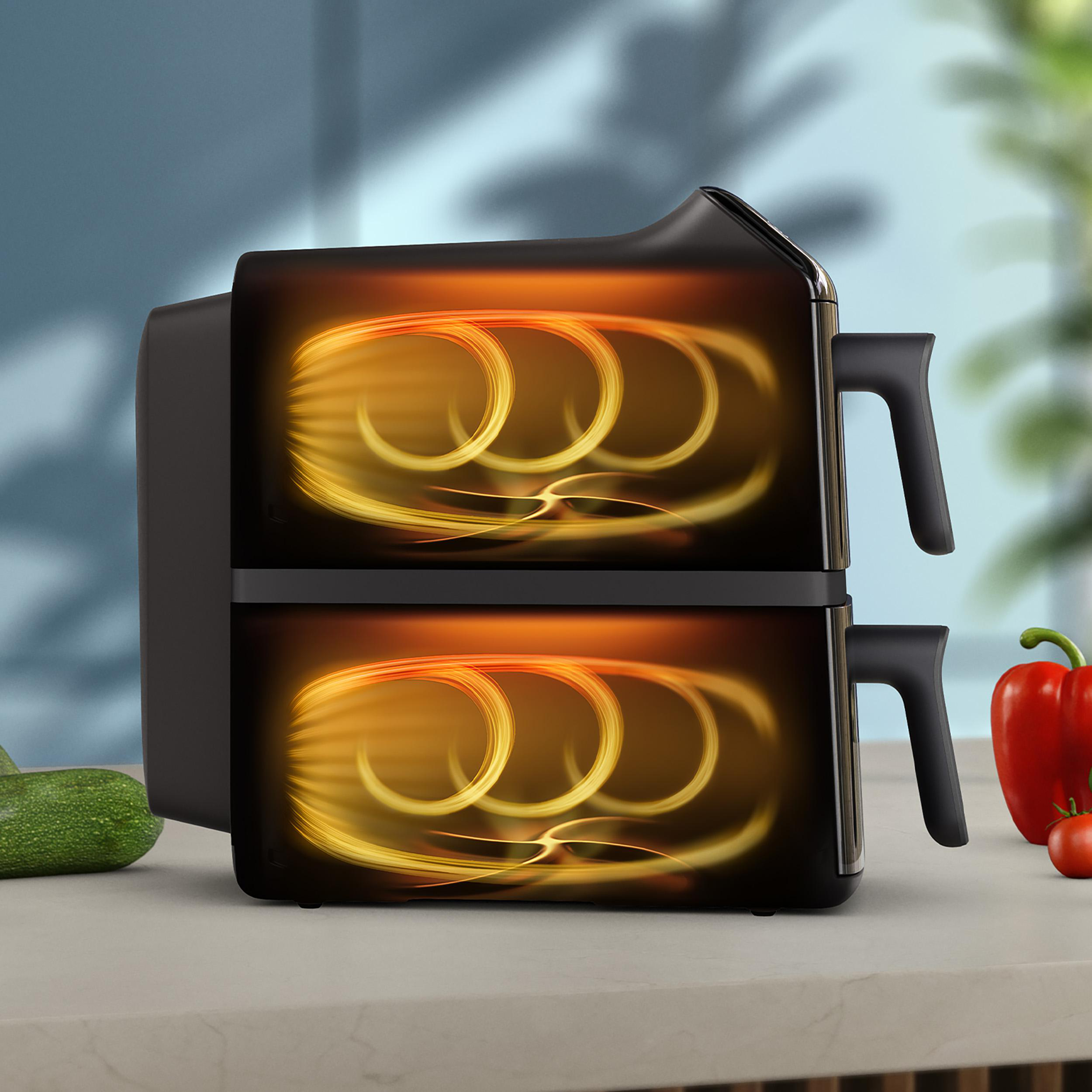 Ein schwarzer Airfryer mit zwei Fächern steht auf einer Theke. Eine Paprika, Tomate und Zucchini sind in der Nähe. Die Innenseite ist beleuchtet.