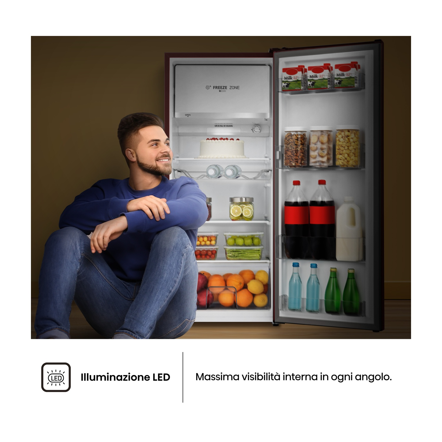 Un uomo seduto vicino a un frigorifero aperto pieno di cibo, che guarda in alto. Il frigorifero contiene latte, soda, frutta e verdura.