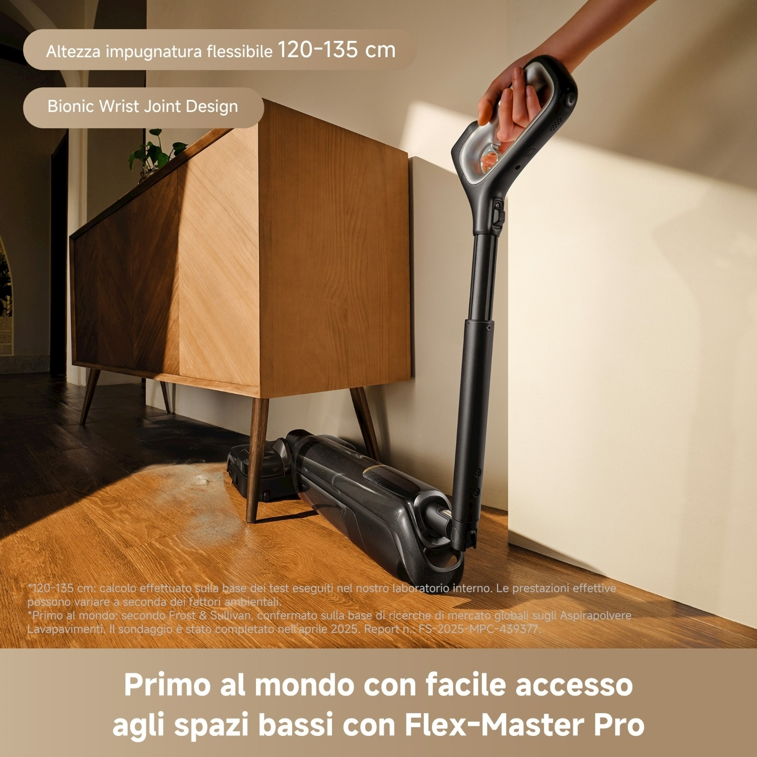 Una persona tiene in mano un aspirapolvere nero, in primo piano, accanto a un mobile in legno su un pavimento in legno. Sovrapposizioni di testo.