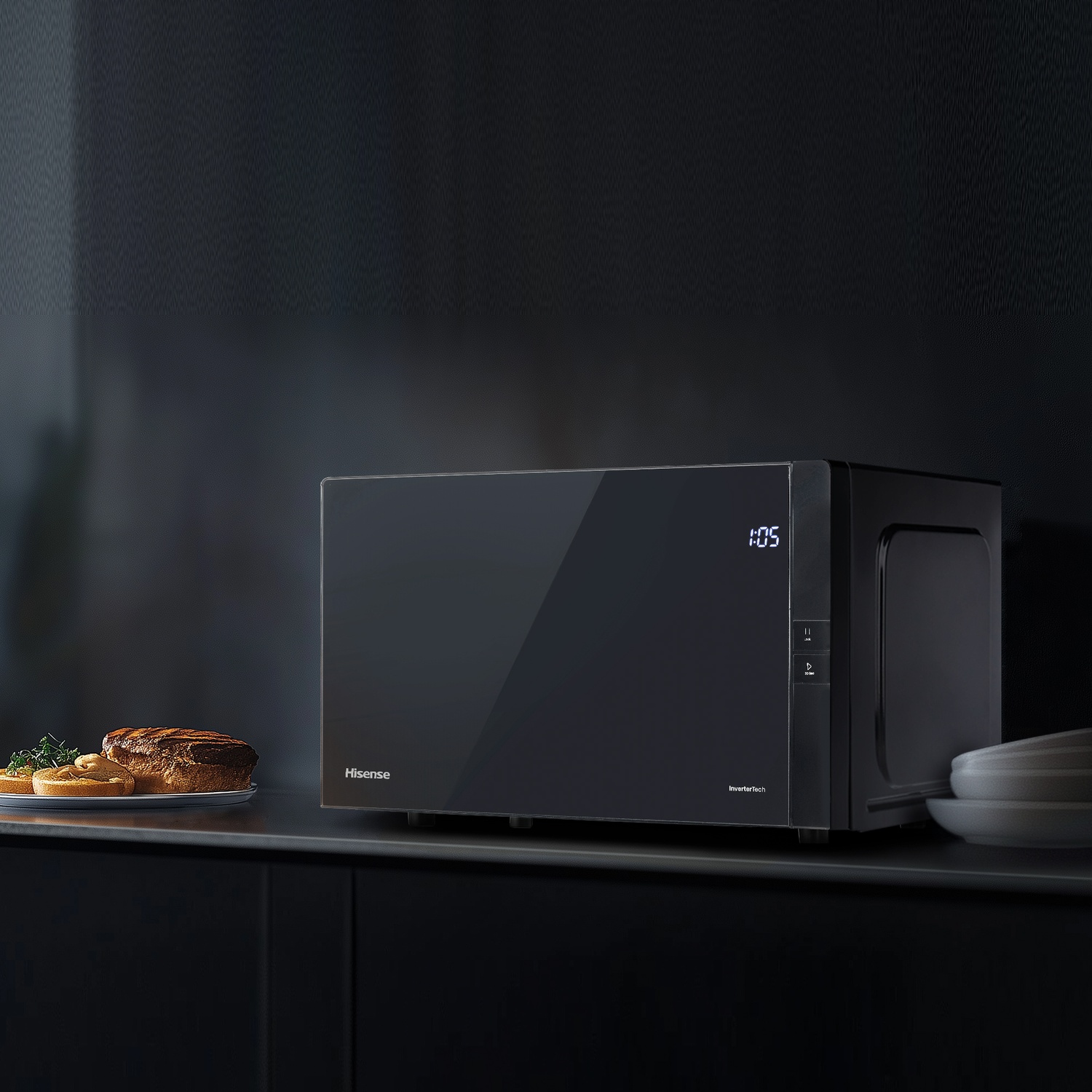 Un forno a microonde Hisense nero è su un bancone con cibo. Lo sfondo è una cucina scura. Il display mostra 1:05.