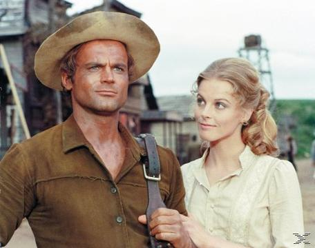Ein Mann mit Cowboyhut und eine Frau in einer Szene. Der Mann trägt ein braunes Hemd, die Frau ein weißes Kleid.