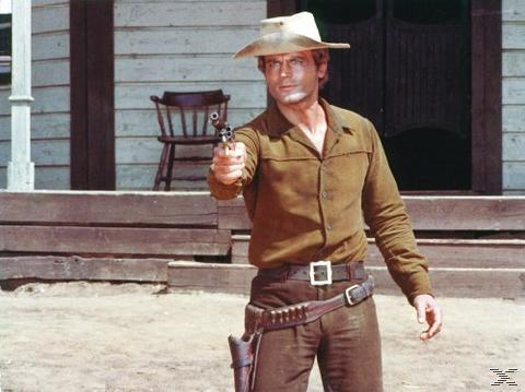 Ein Mann mit Cowboyhut und braunem Hemd zielt mit einer Pistole. Er steht vor einem Holzgebäude.