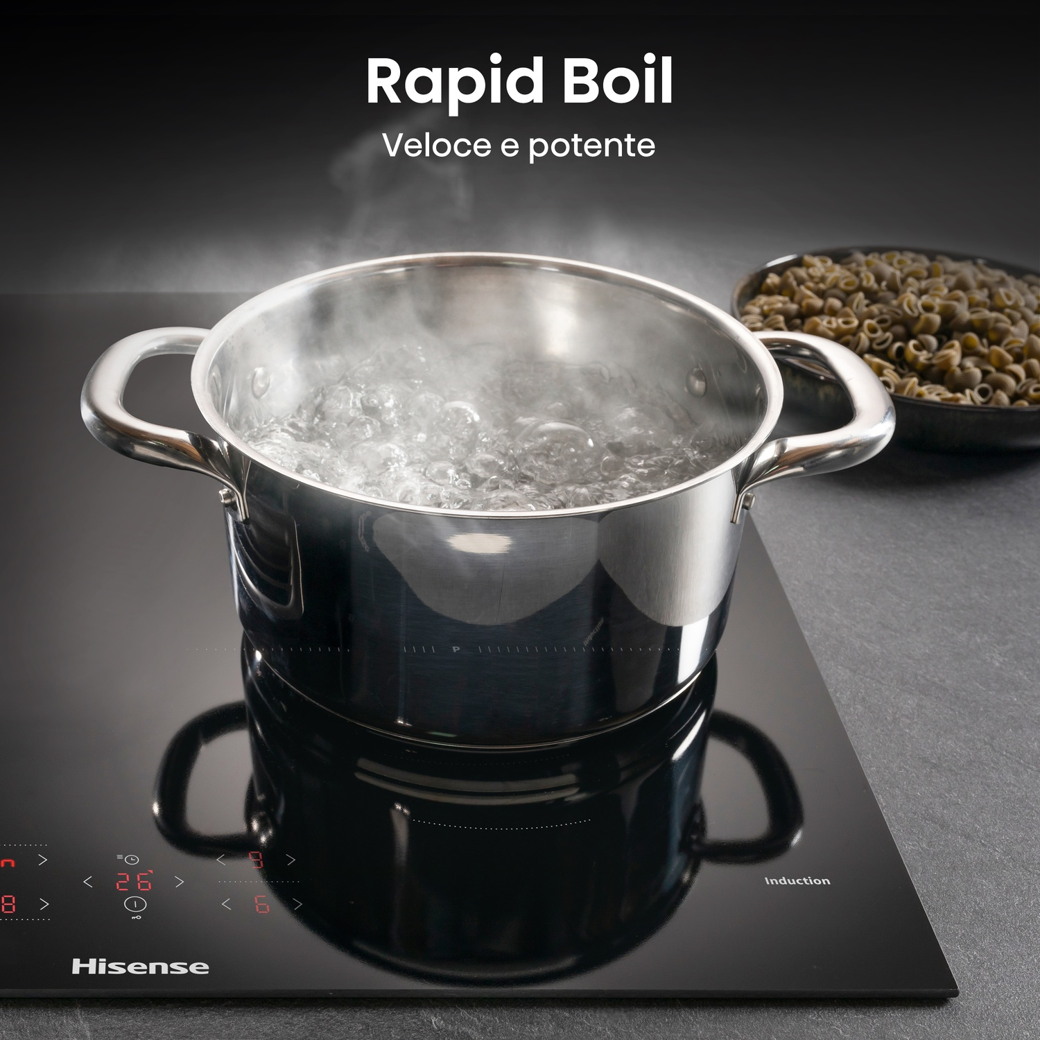 Una pentola di acqua bollente è su un piano cottura a induzione nero. Il vapore sale e una ciotola di pasta è sullo sfondo.