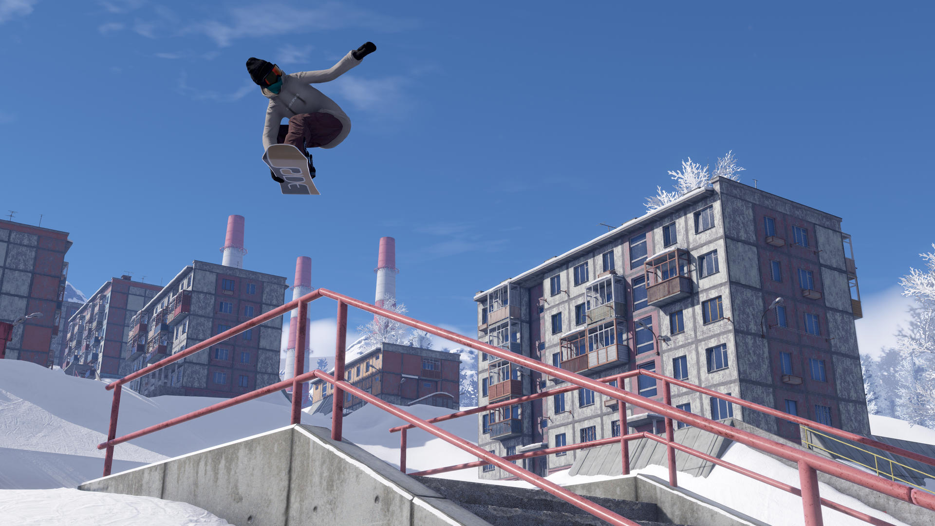 Ein Snowboarder führt einen Trick in der Luft vor dem Hintergrund von Gebäuden, Schornsteinen und einem klaren blauen Himmel aus. Schnee bedeckt den Boden.
