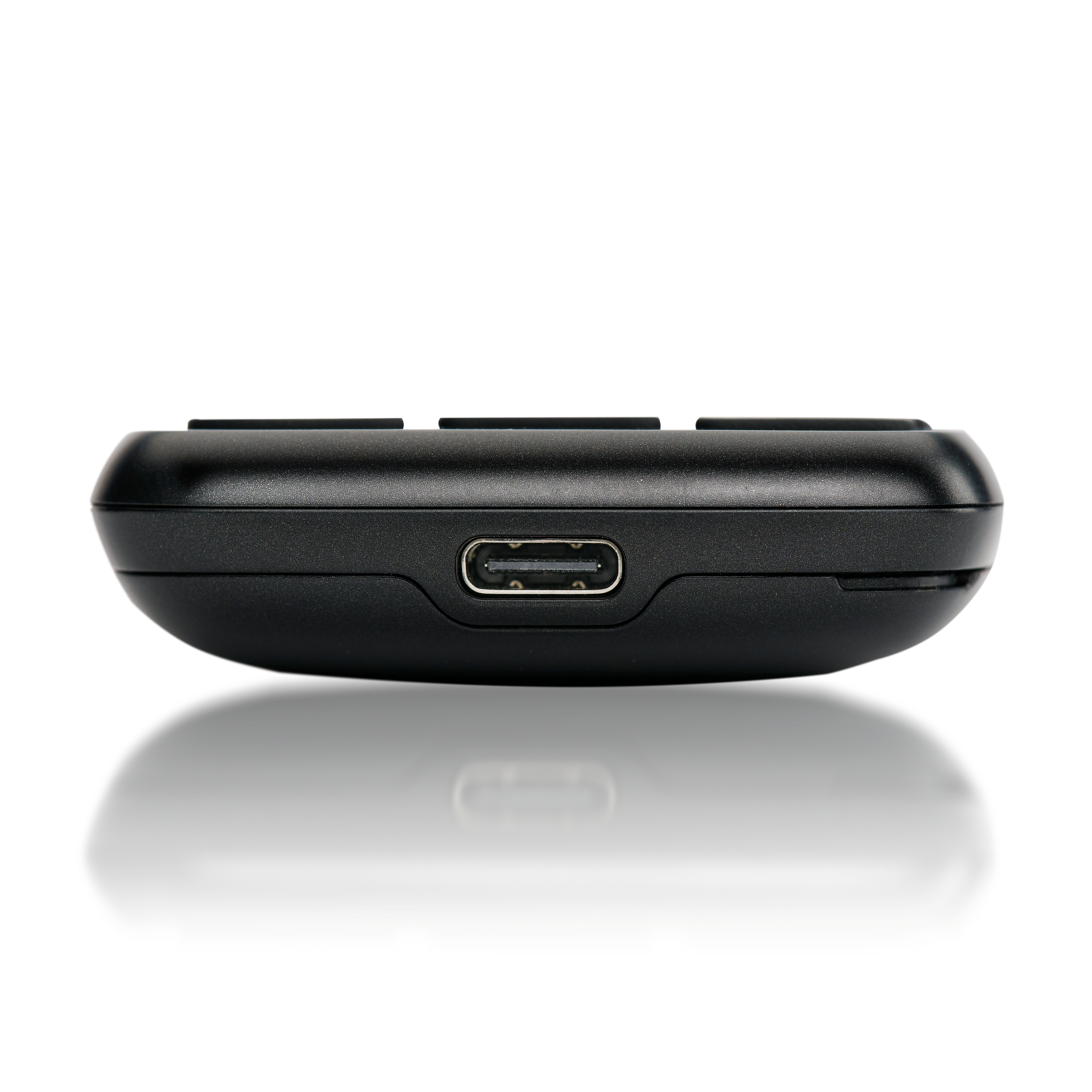 Egy fekete eszköz oldala, USB-porttal és gombokkal. Az eszköz árnyékot vet egy fehér felületre.