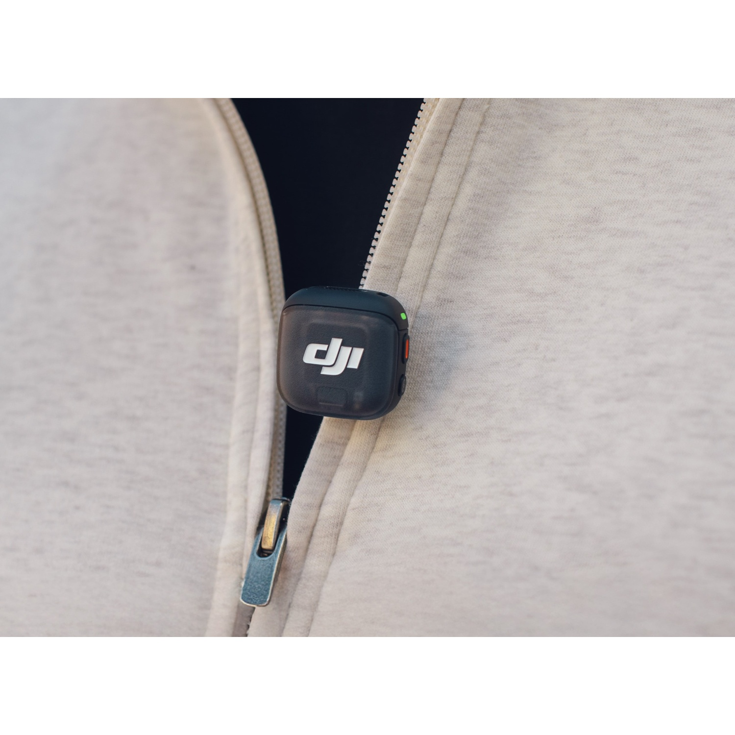 Een zwarte DJI-microfoon is vastgeklikt aan een lichtgrijze hoodie. De rits is gedeeltelijk gesloten.