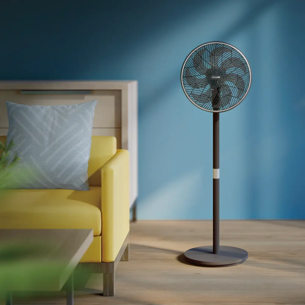 Un ventilador de pie, un sofá amarillo con una almohada y una mesa de madera. Una pared azul está en el fondo. El suelo es de madera.