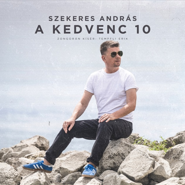 Férfi napszemüvegben sziklákon ül. Fehér pólót, fekete nadrágot és kék cipőt visel. Az égbolt és a lemezcím látható.