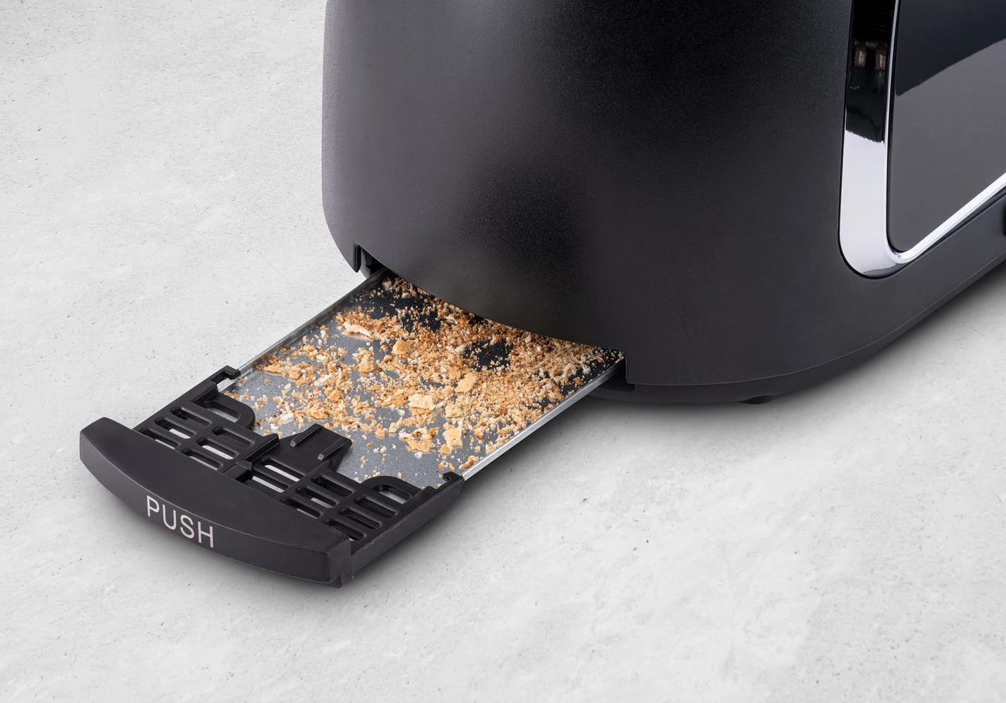 Un grille-pain noir avec un tiroir ramasse-miettes rempli de miettes. Le tiroir est étiqueté « PUSH ».