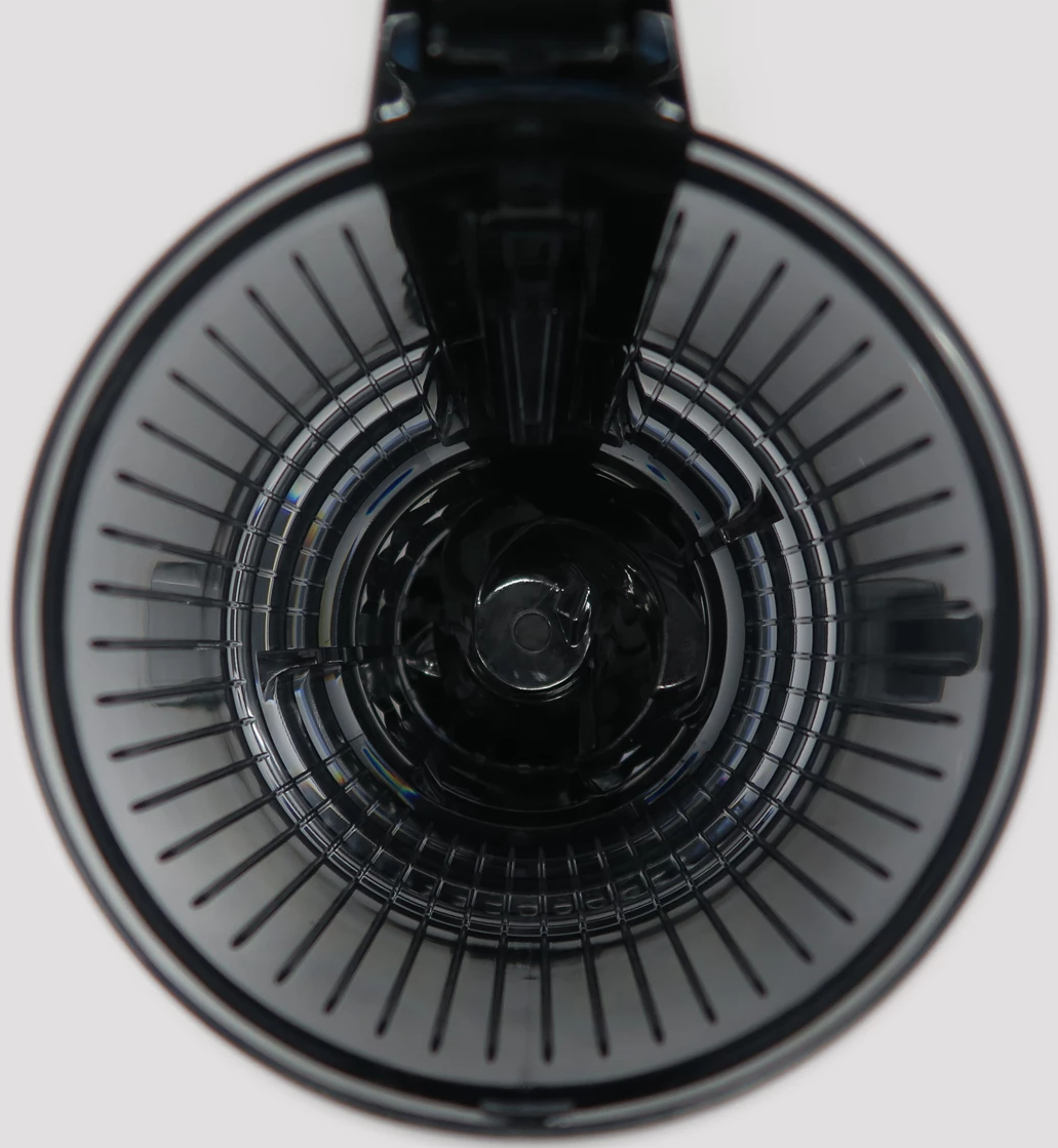 Vista dall'alto dell'interno di un'estrattore di succo nero. Ha un design circolare con barre verticali. Lo sfondo è bianco.