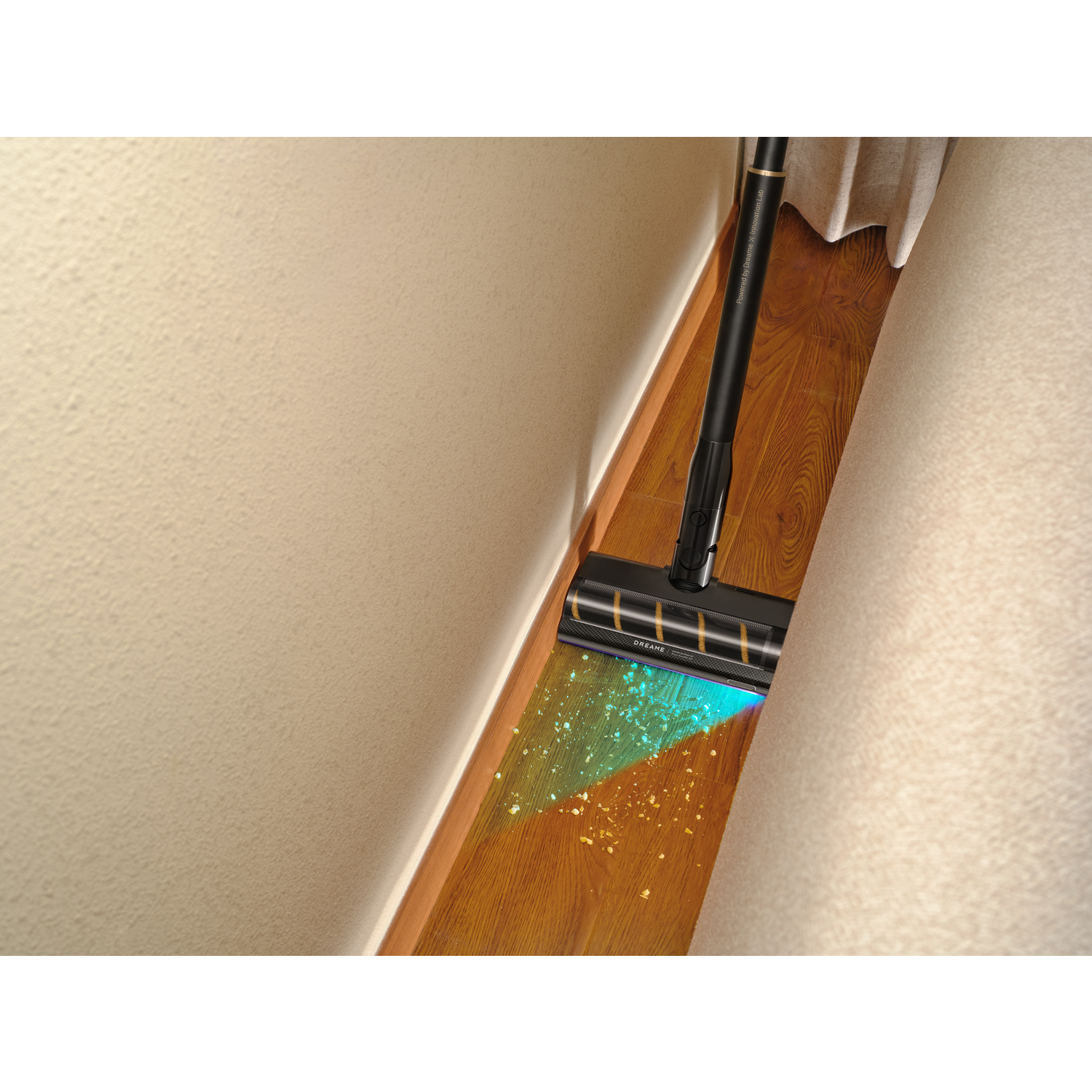 A black vacuum cleaner cleaning a wooden floor. The floor has visible dust. The vacuum is near a wall and a curtain.