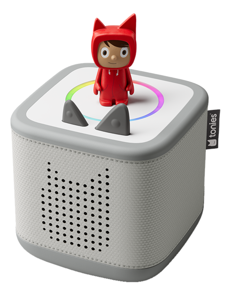 Une figurine à capuche rouge se tient sur un haut-parleur gris. Le haut-parleur a un dessus blanc avec deux oreilles grises et un anneau arc-en-ciel.