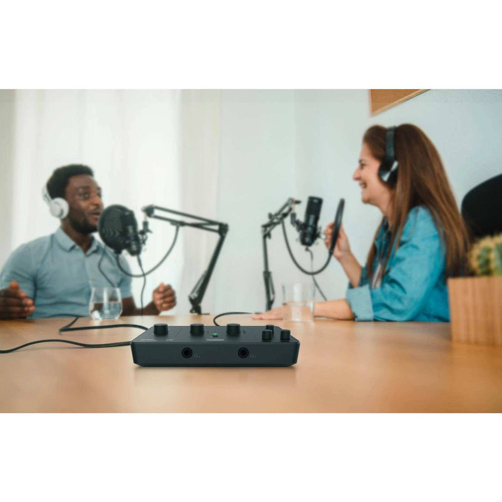 Dos personas haciendo un podcast con micrófonos y auriculares. Una mesa con un mezclador de audio negro en primer plano.